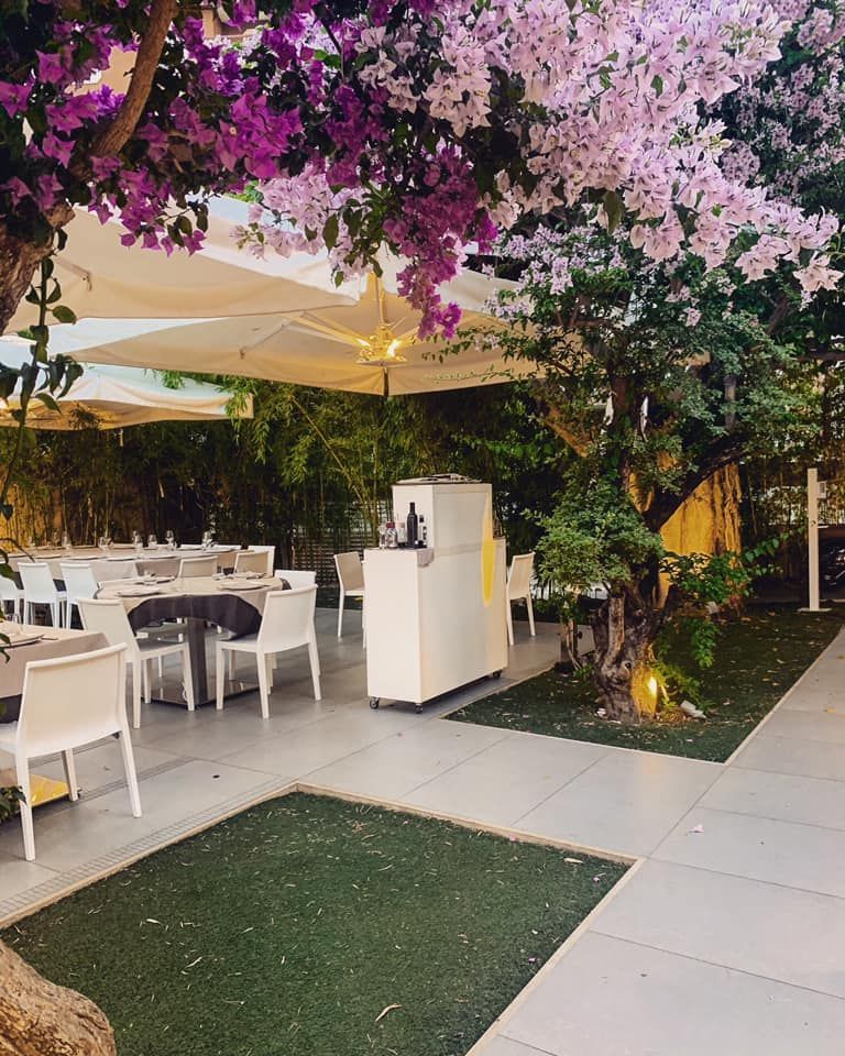 Un patio con tavoli e sedie sotto gli ombrelloni e un albero dai fiori viola.