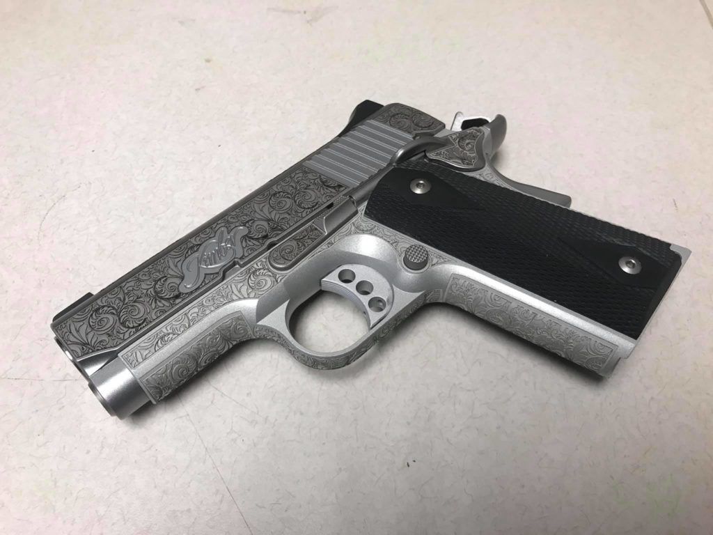 Silver and black handgun with patterned slide on a light surface
