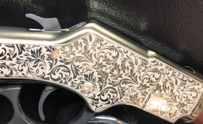 Close-up of an ornate silver-patterned revolver grip with floral engraving against a black background