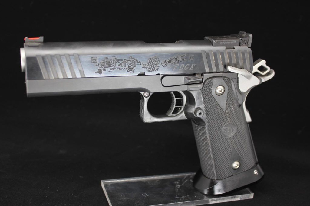 Black semi-automatic pistol with engraved slide on a display stand against a plain background