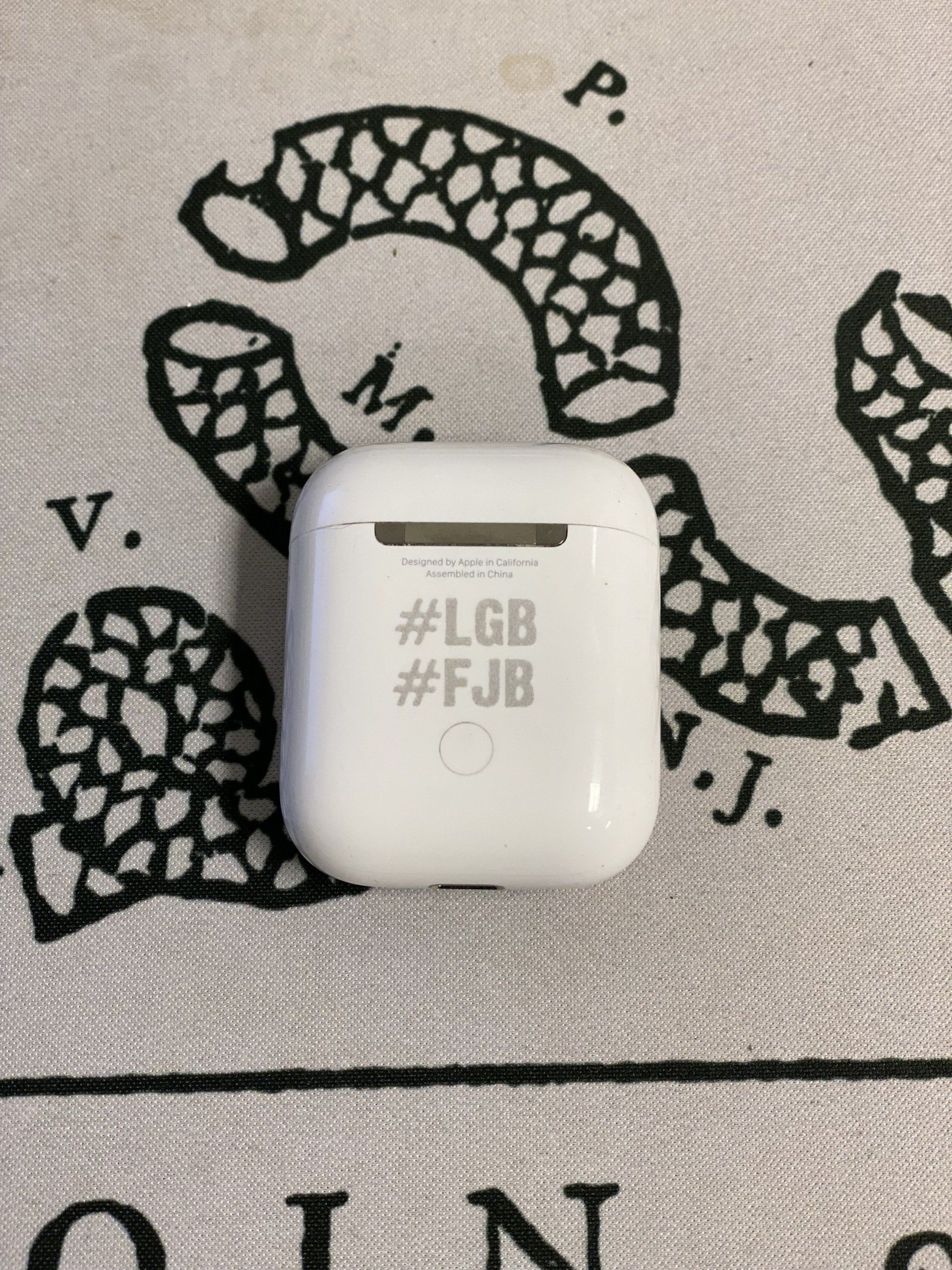 White wireless earbuds case on patterned fabric with black text and decorative designs.