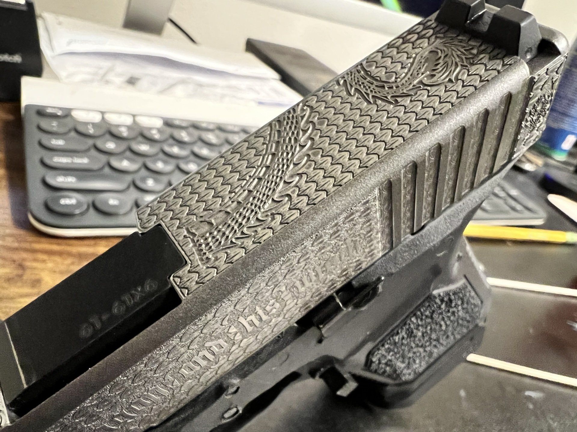 Black textured handgun on a desk with a smartphone and keyboard in the background