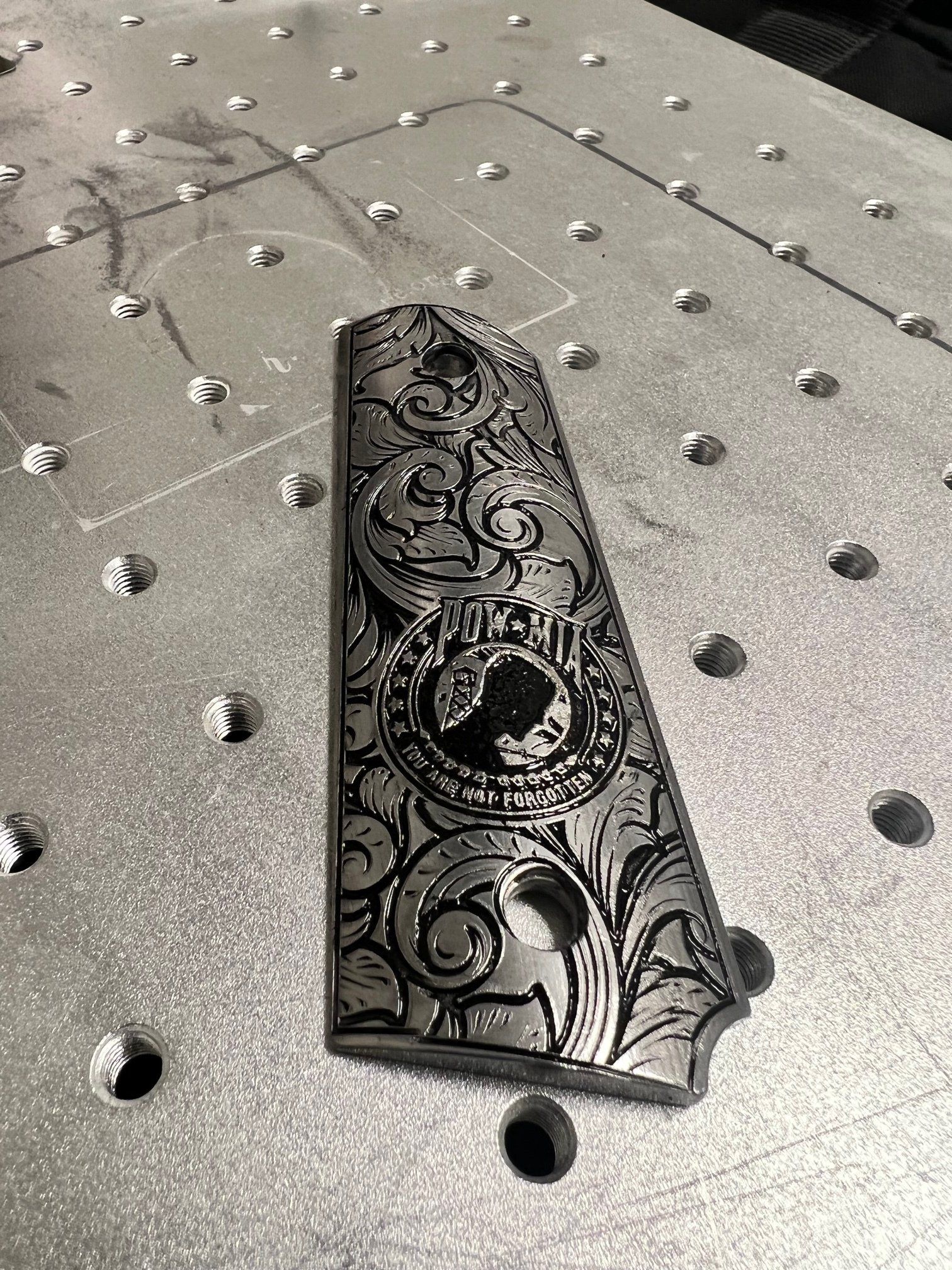 Black ornate engraved metal piece on a perforated gray work surface.