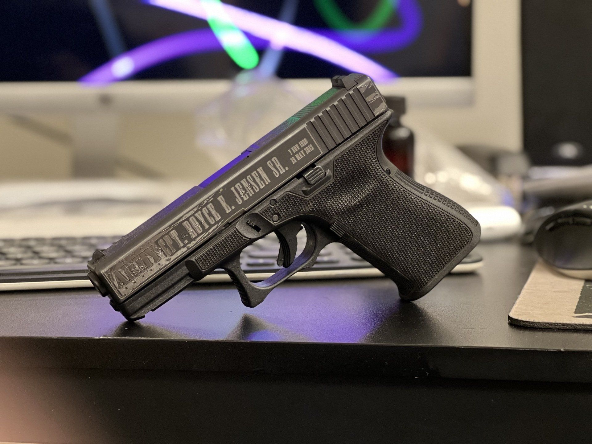 Glock handgun on a desk. Etched details visible on the slide and grip, in a home or office setting.