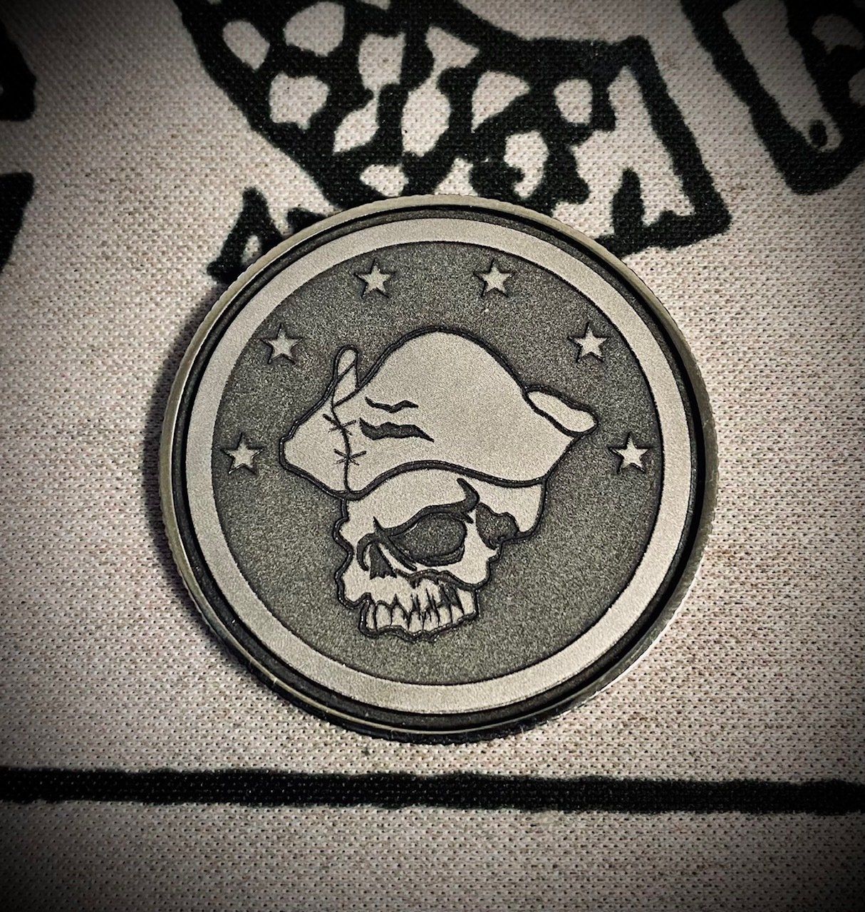A skull emblem patch with a hat, stitched on beige fabric with black patterns.