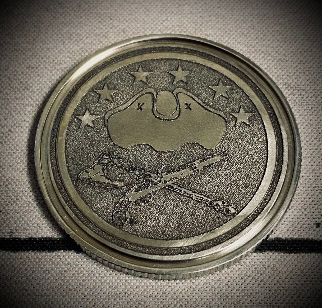 Circular metal medallion with a bat-like emblem and star pattern on a textured surface