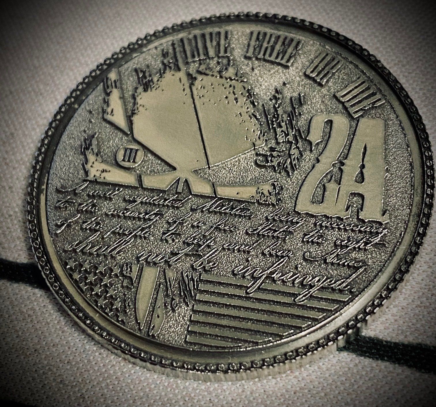 Close-up of a round engraved metal medallion with a tree, landscape, and geometric patterns