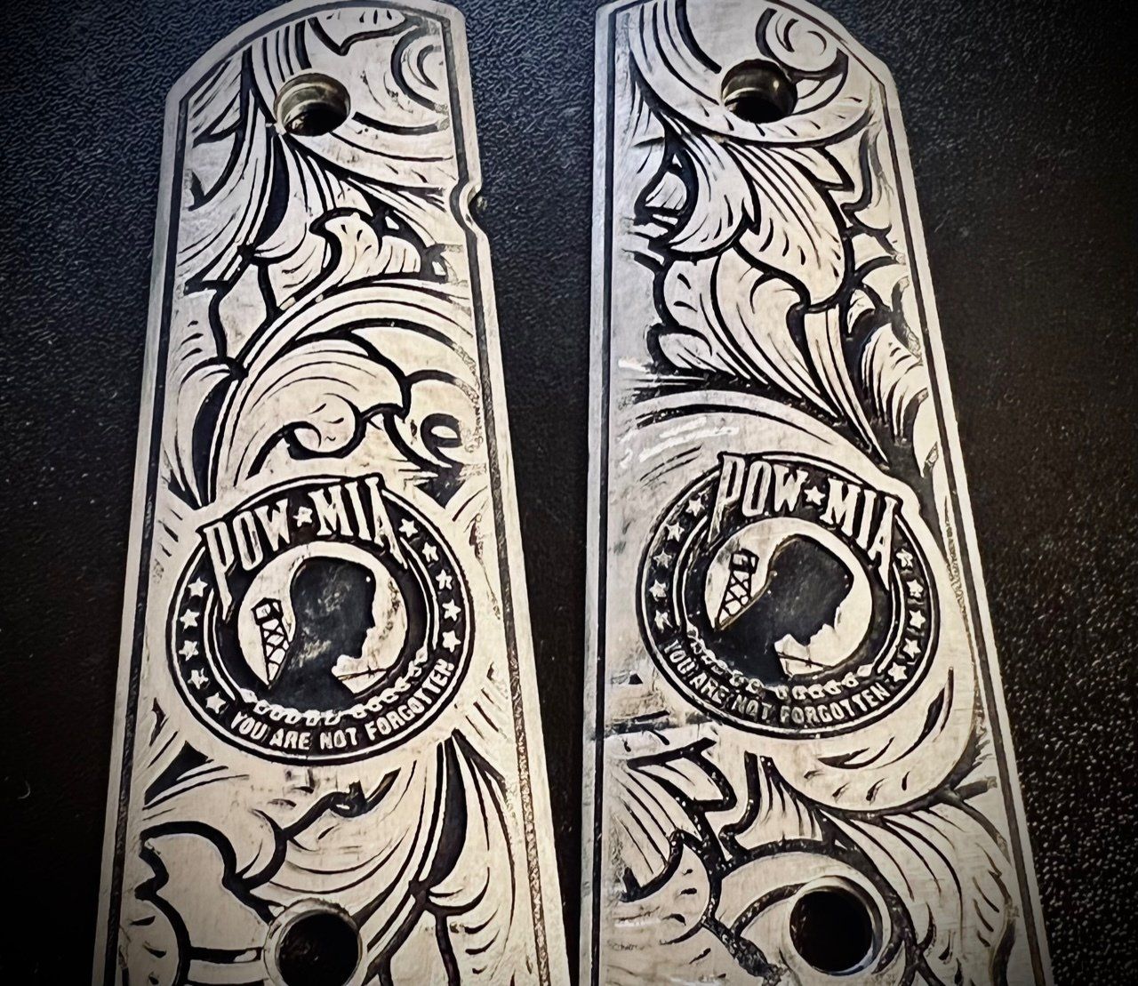 Two ornate black-and-white engraved panels with floral scrollwork and circular medallions on a dark surface