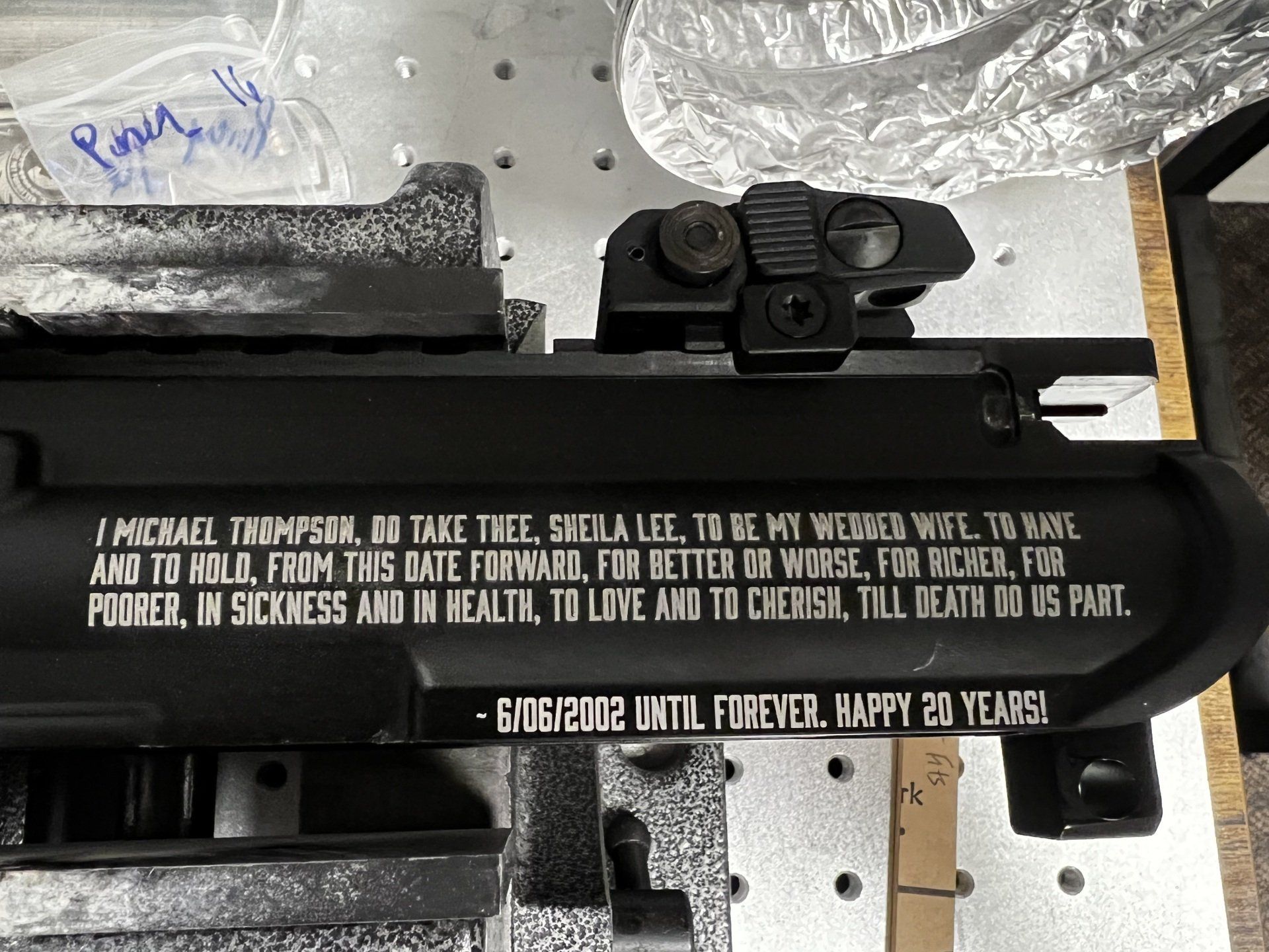 Black sign with white text mounted on machinery, viewed from above on a workshop table.