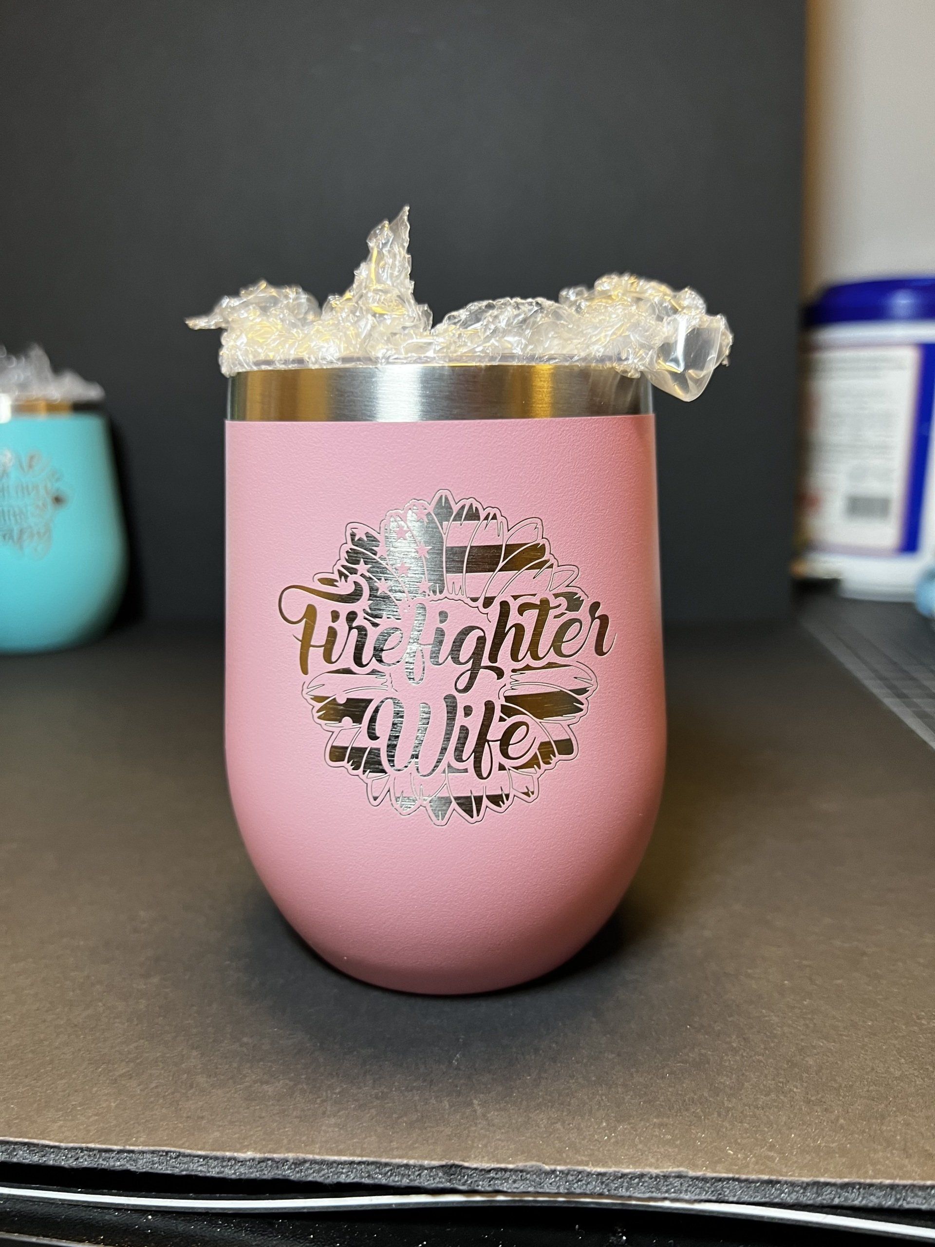 Pink insulated tumbler with silver rim and glittery garnish on a black tabletop.