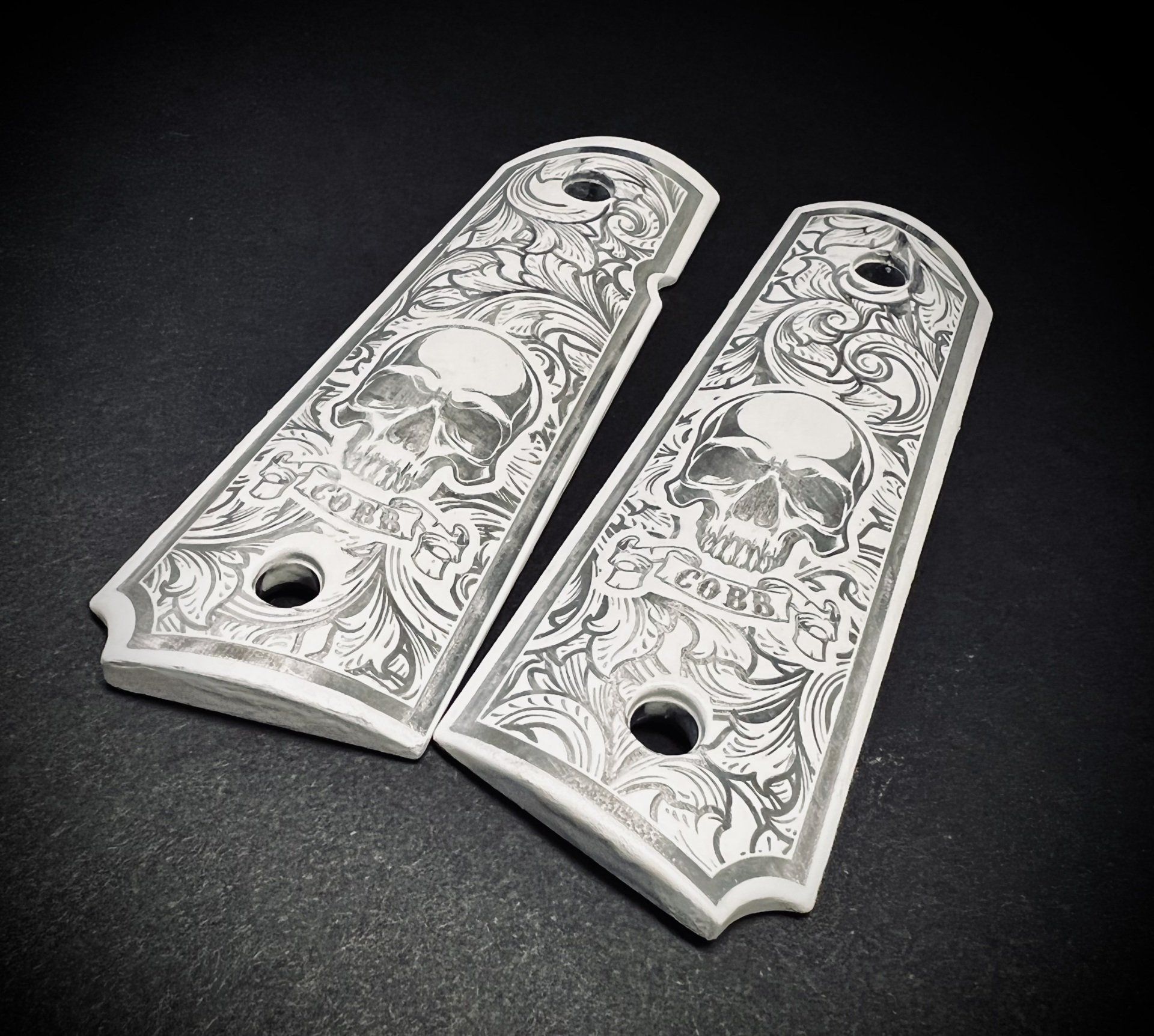 Two white engraved pistol grips with skull design and floral details.