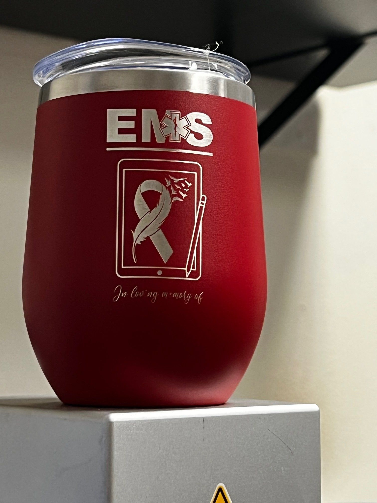 Red insulated tumbler with silver ribbon logo and EMS text on a white surface
