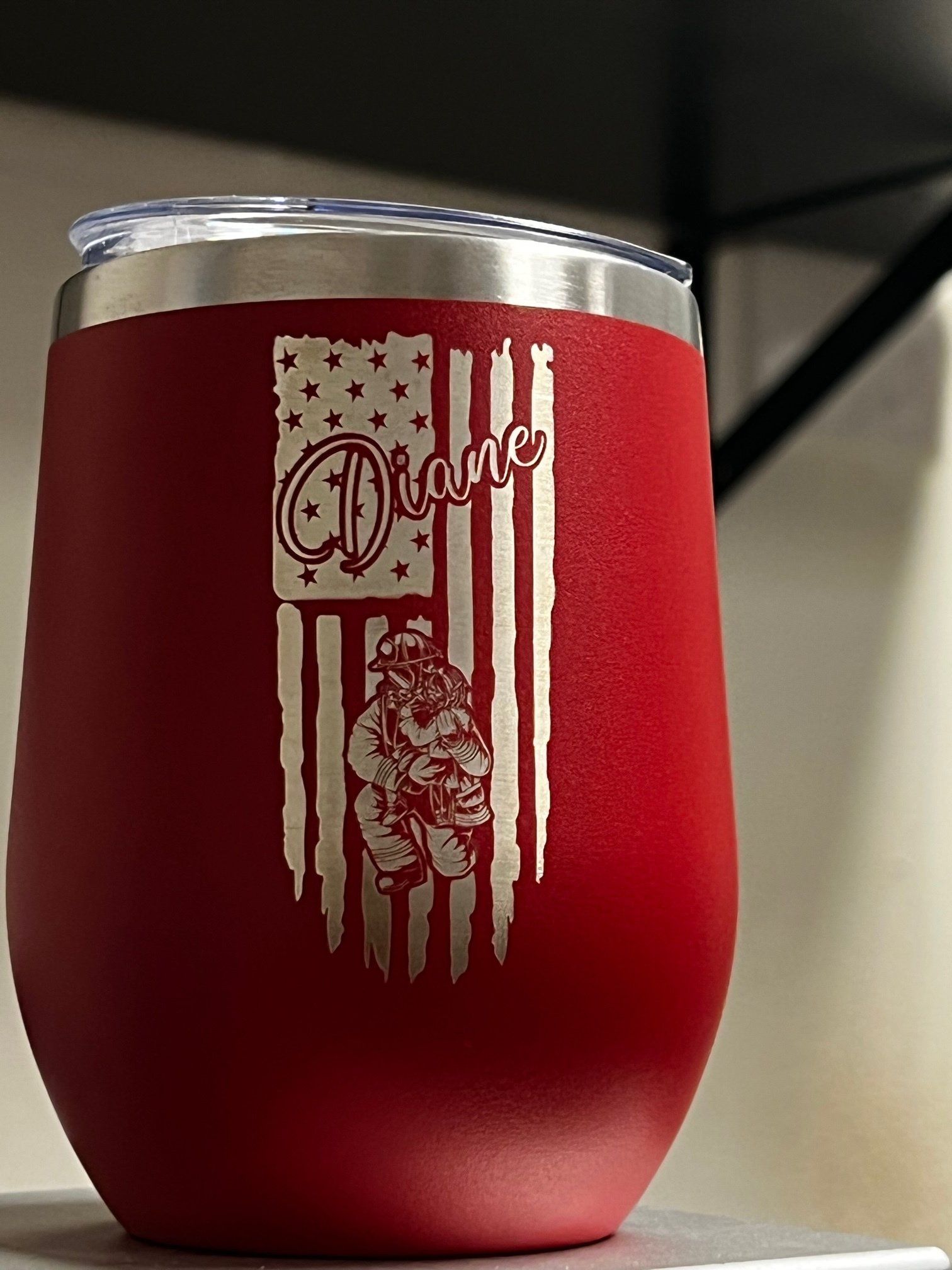Red tumbler with silver rim and white patriotic flag design on the front.