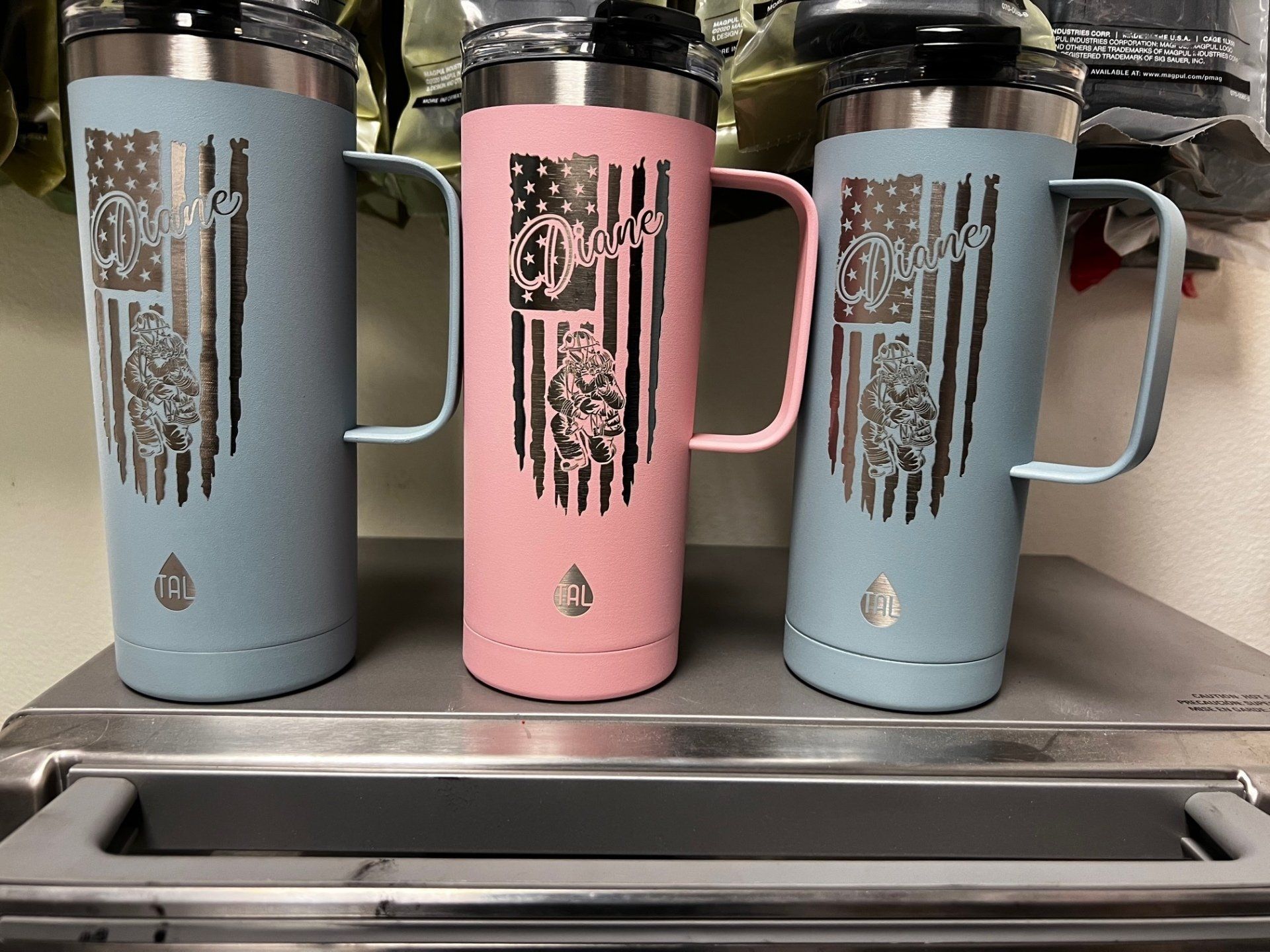 Three insulated tumblers in blue, pink, and light blue on a countertop near a sink.