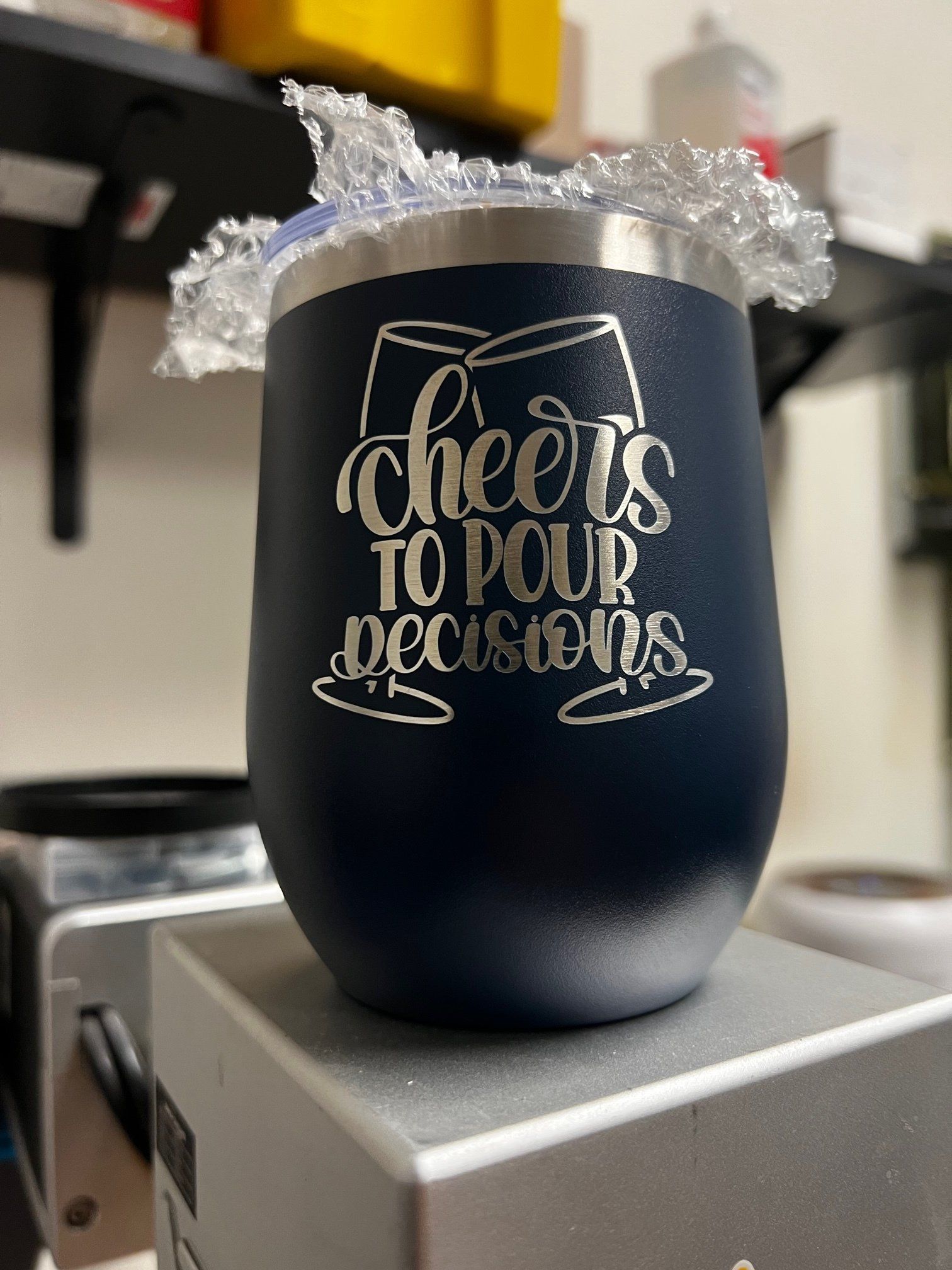 Navy insulated tumbler with “cheers to new beginnings” on a countertop, topped with clear decorative wrap.