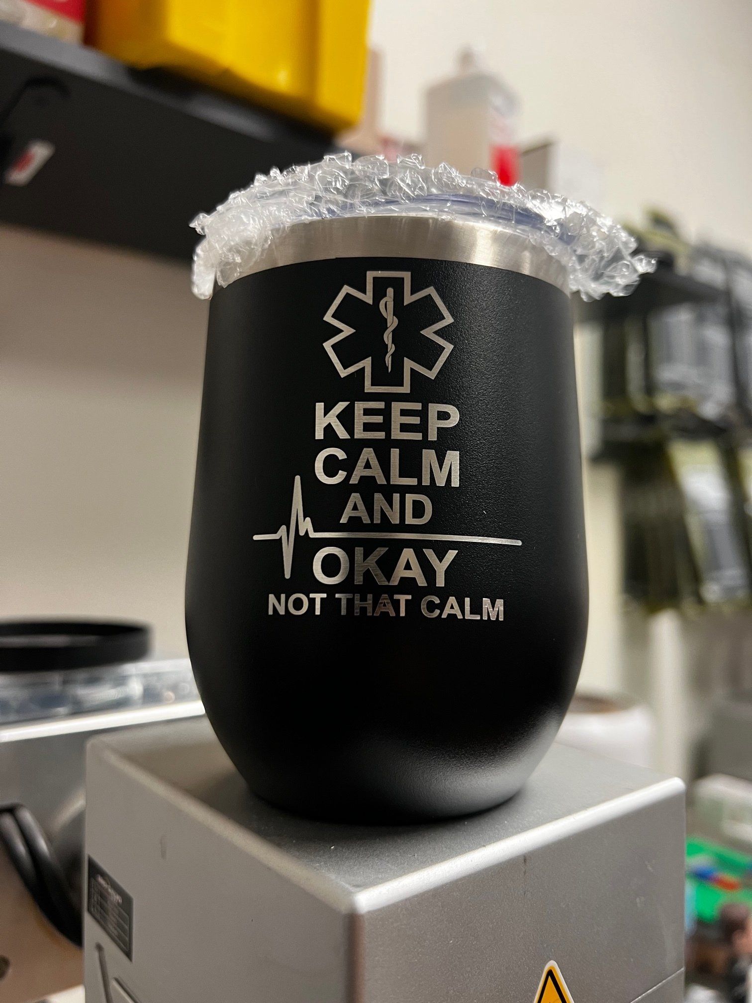 Black tumbler with “Keep Calm and Okay Not That Calm” text, wrapped in clear bubble wrap on a box.