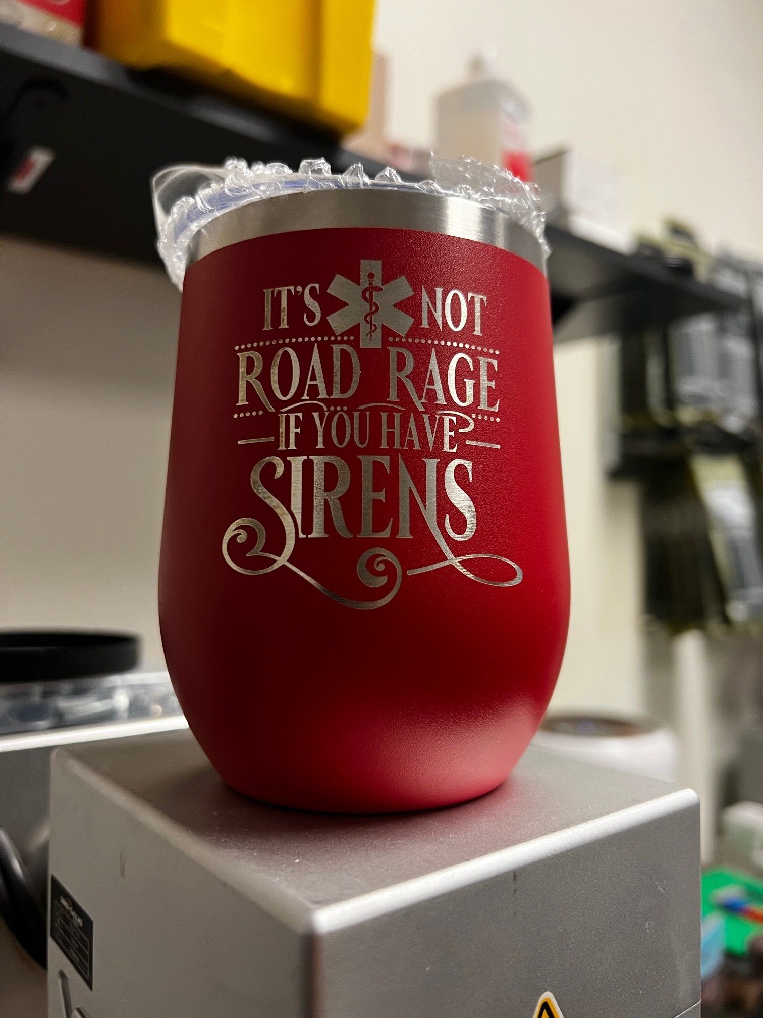 Red insulated tumbler with white holiday text and a lace rim sitting on a gray box.