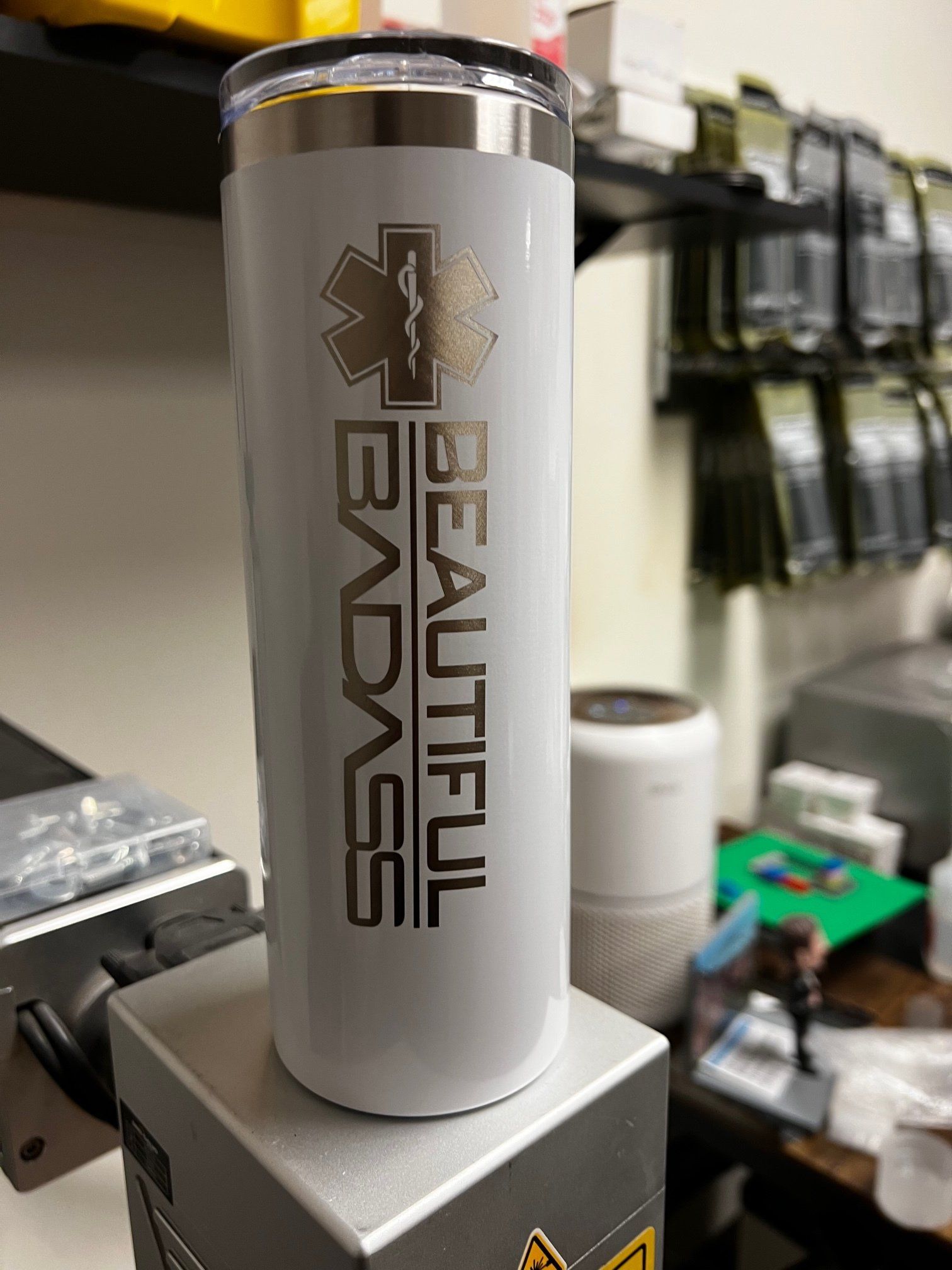 White tumbler with black “Beautiful Badass” text on a counter in a shop