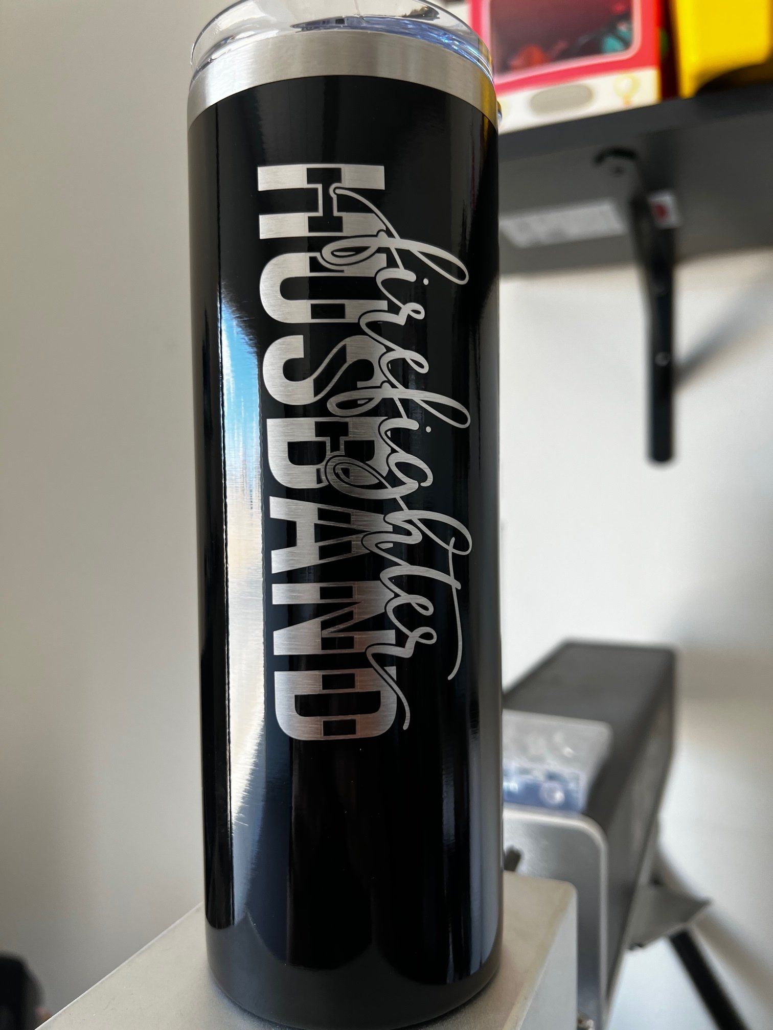 Black tumbler with silver “Hustland” text on a desk in an indoor setting