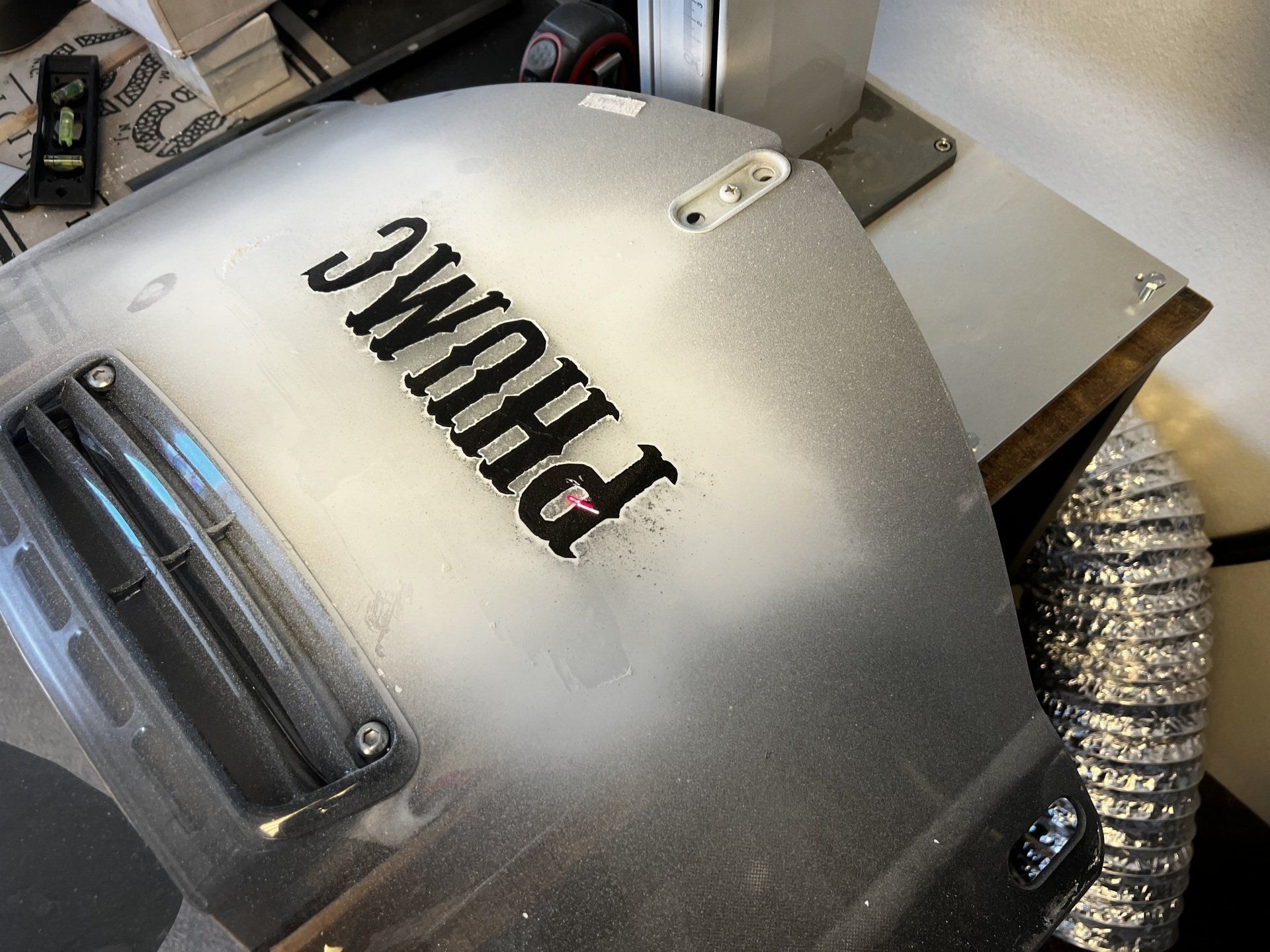 Close-up of a silver helmet with black lettering and a clear visor on a workbench