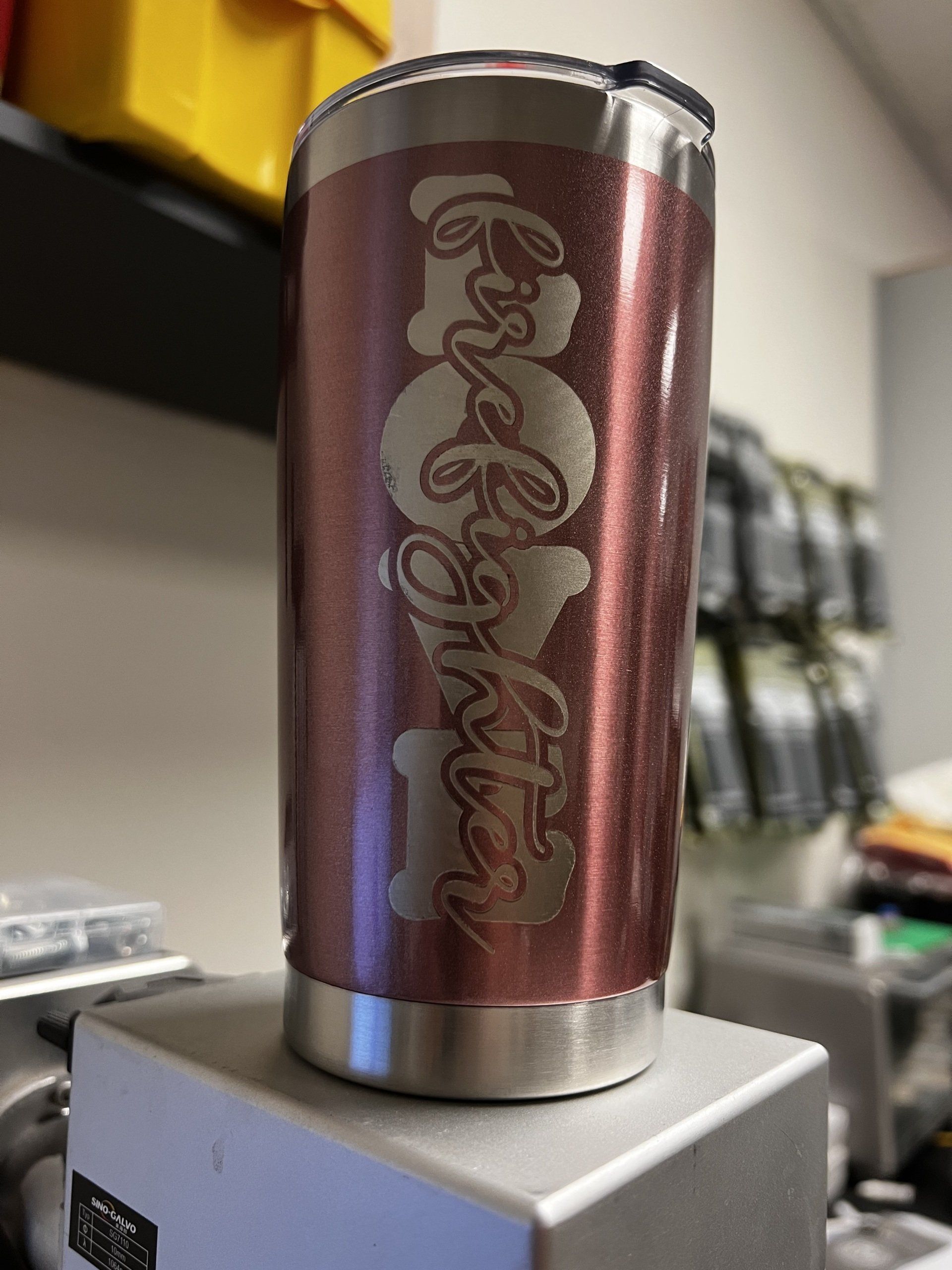 Maroon insulated tumbler with vertical decorative script on a white box, on a tabletop.