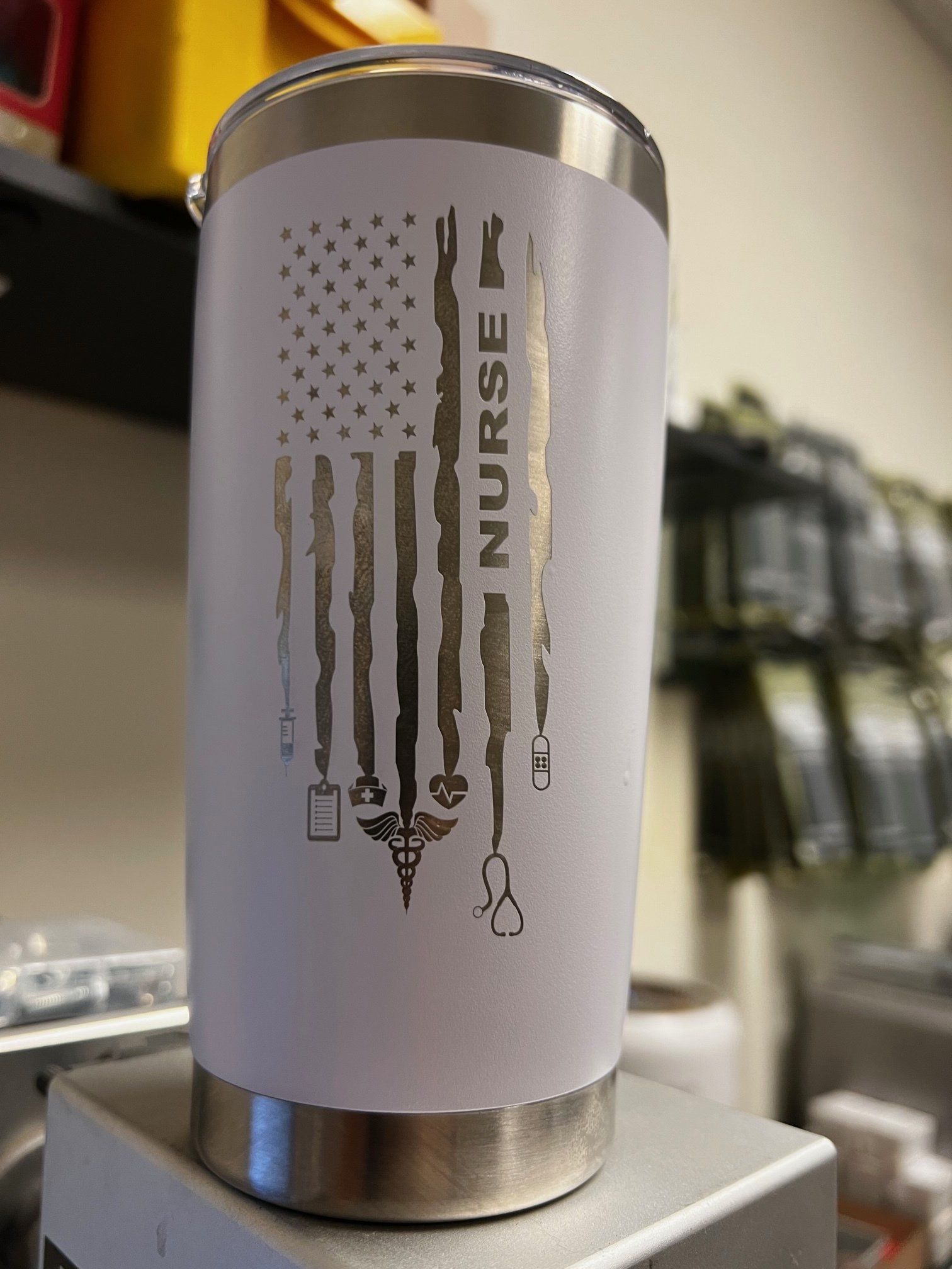 White tumbler with distressed American flag and “NURSE” text on a metal stand.