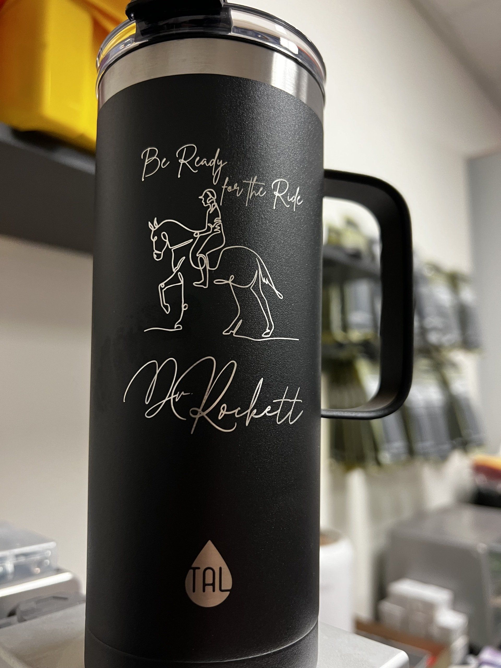 Black insulated travel mug with white text and line art on a kitchen counter.