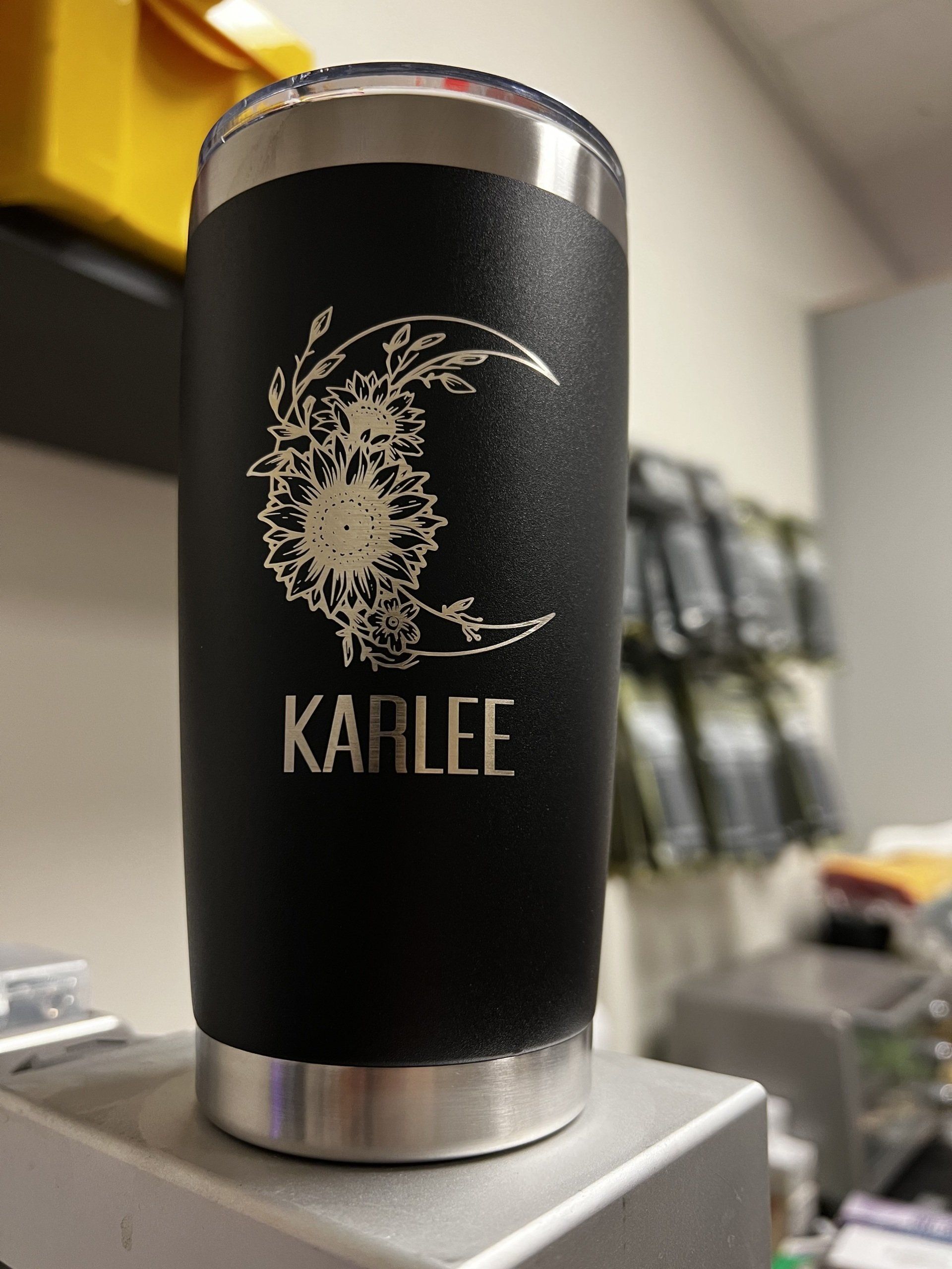 Black insulated tumbler with a silver floral design and the name “KARLEE” on a counter.
