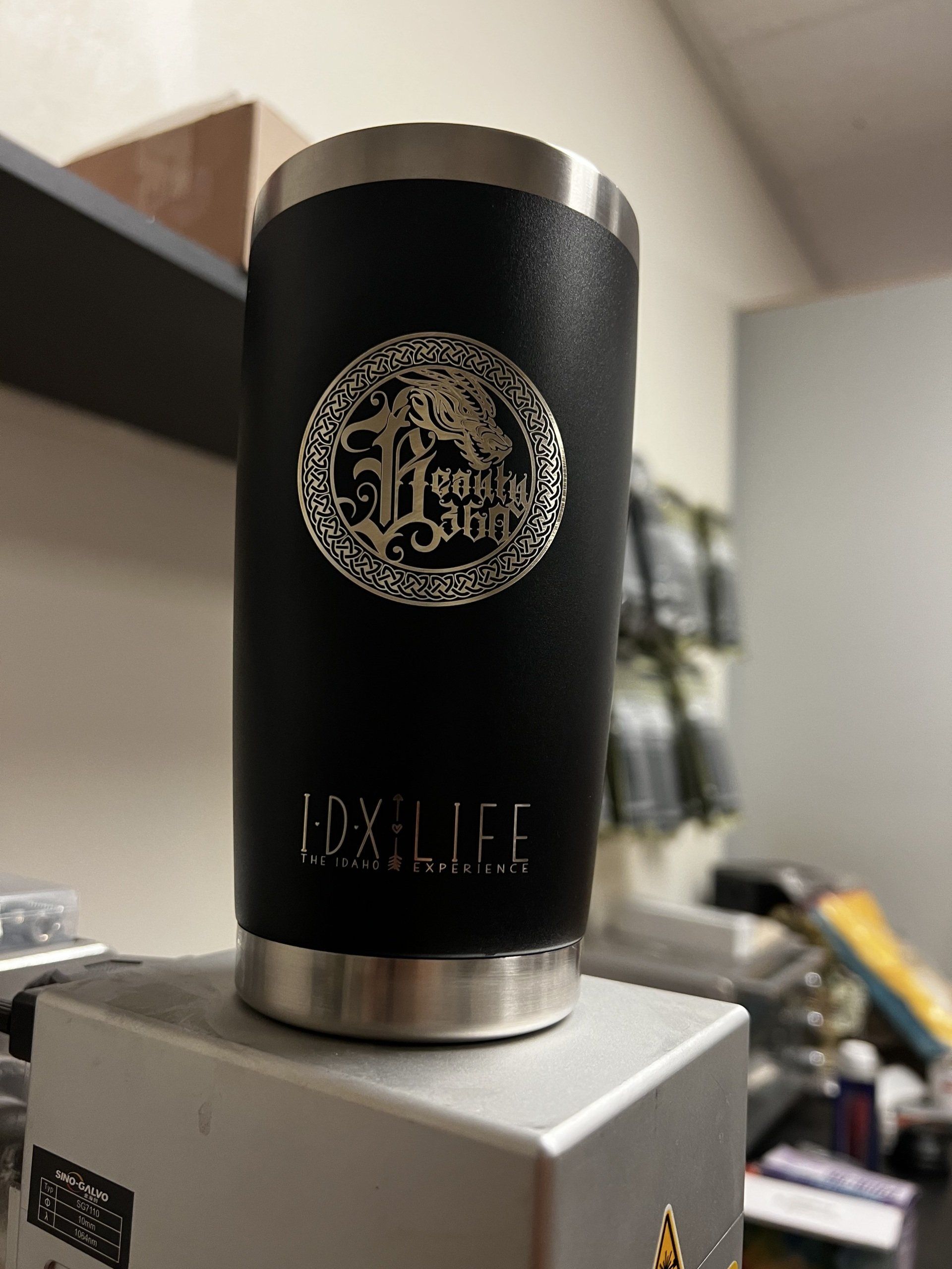 Black cylindrical bottle with gold emblem on a silver box in an indoor setting