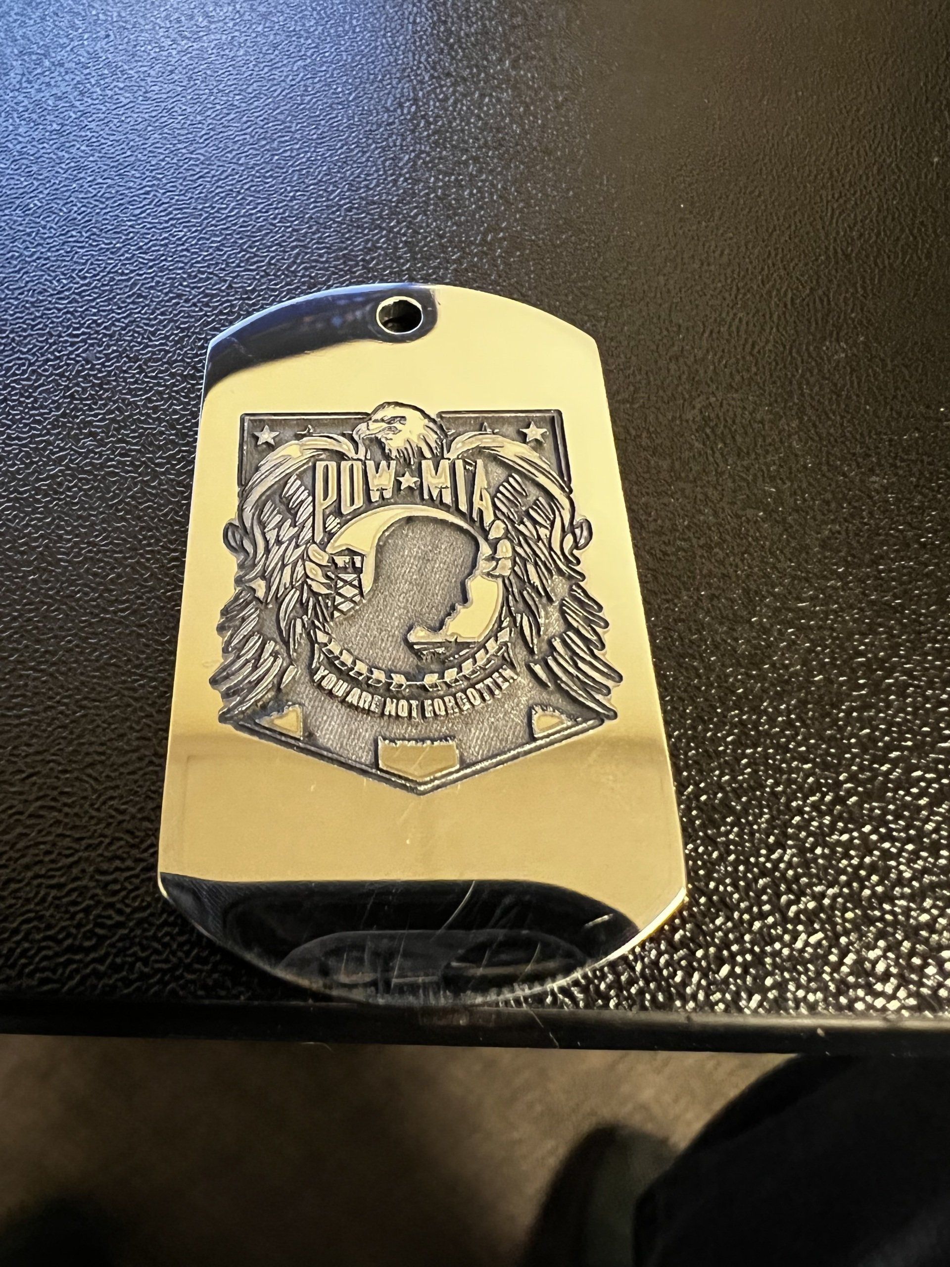 Gold dog tag-style pendant with a black crest design on a dark textured surface