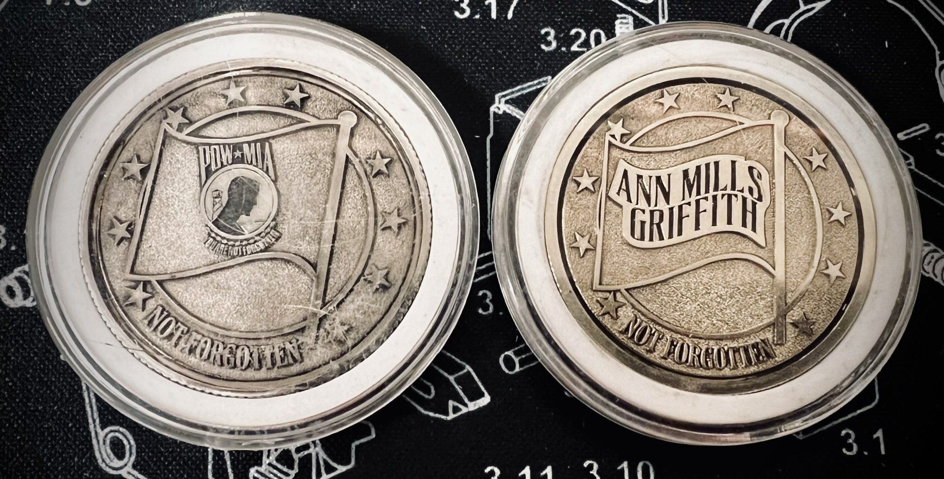 Two silver coins on a dark background, one showing a crest and the other a banner with text.