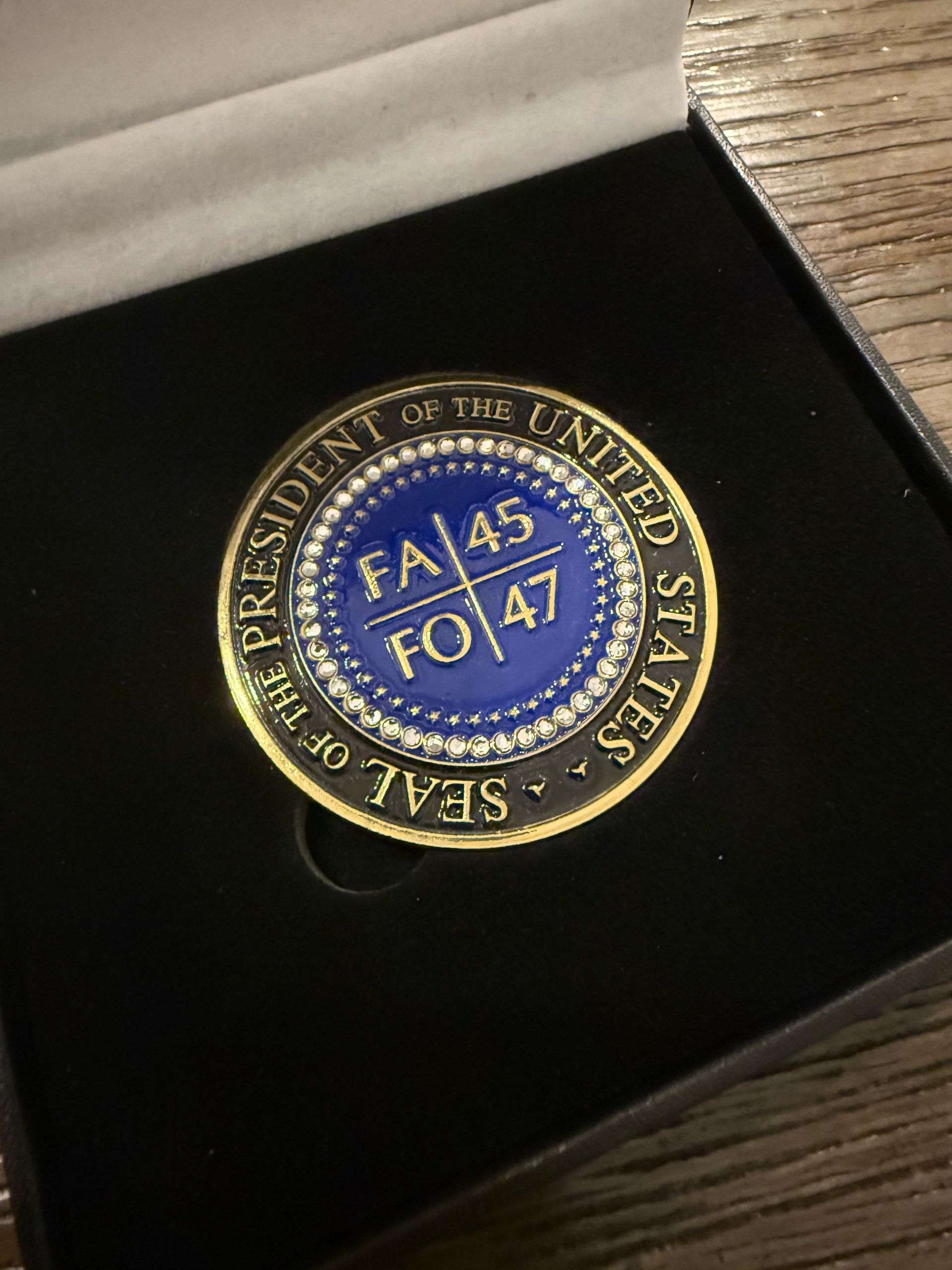 Close-up of a blue and gold circular pin or medallion in a black box with white satin lining
