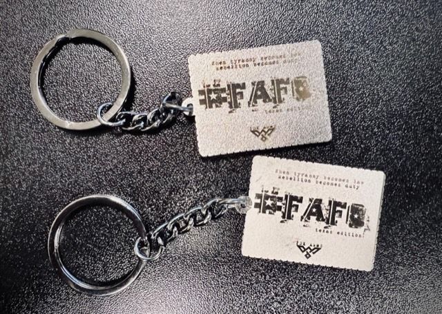 Two silver keychains with square tags featuring text and a hashtag.