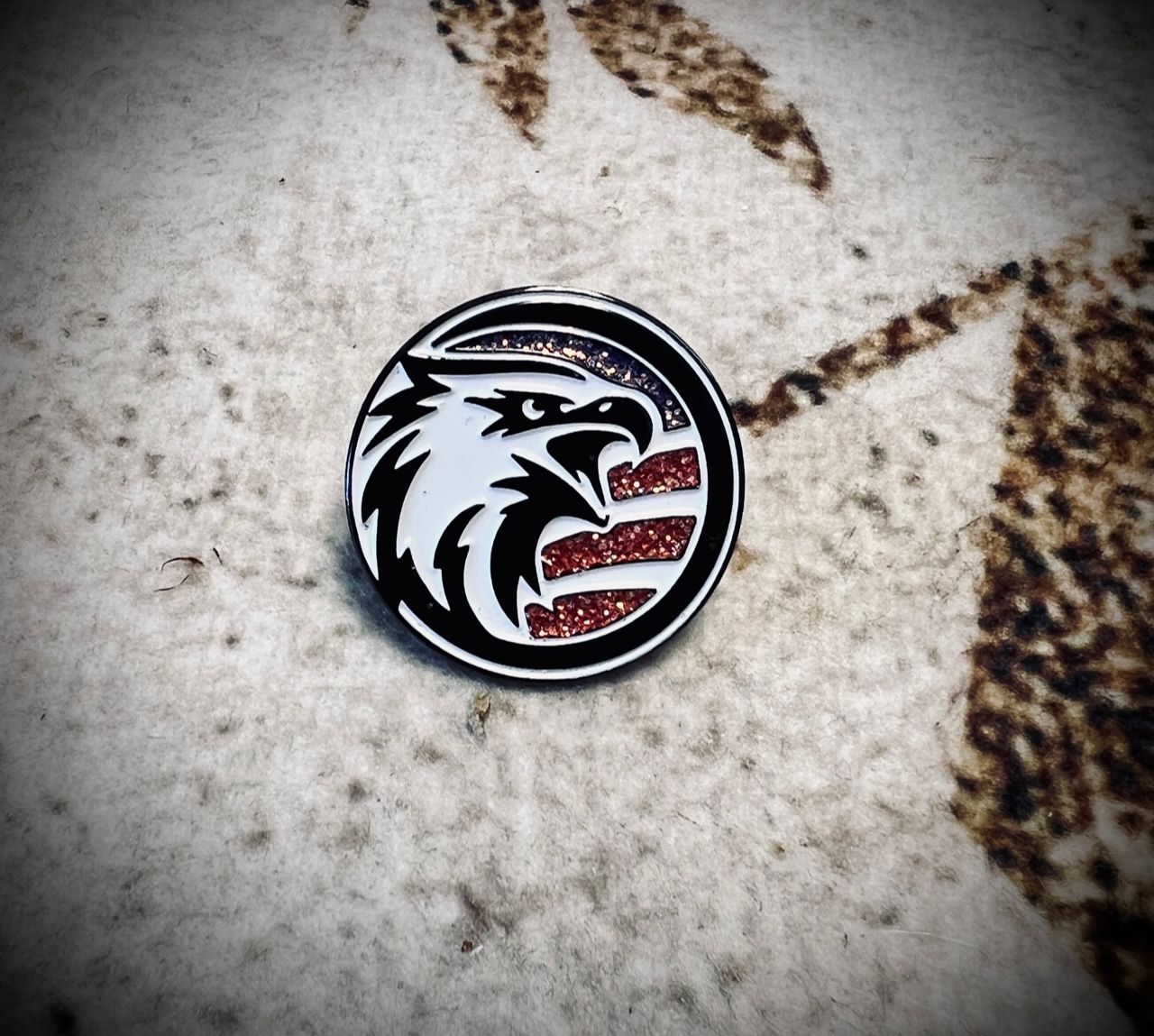Circular black-and-white wolf logo pin with red accents on a light patterned surface