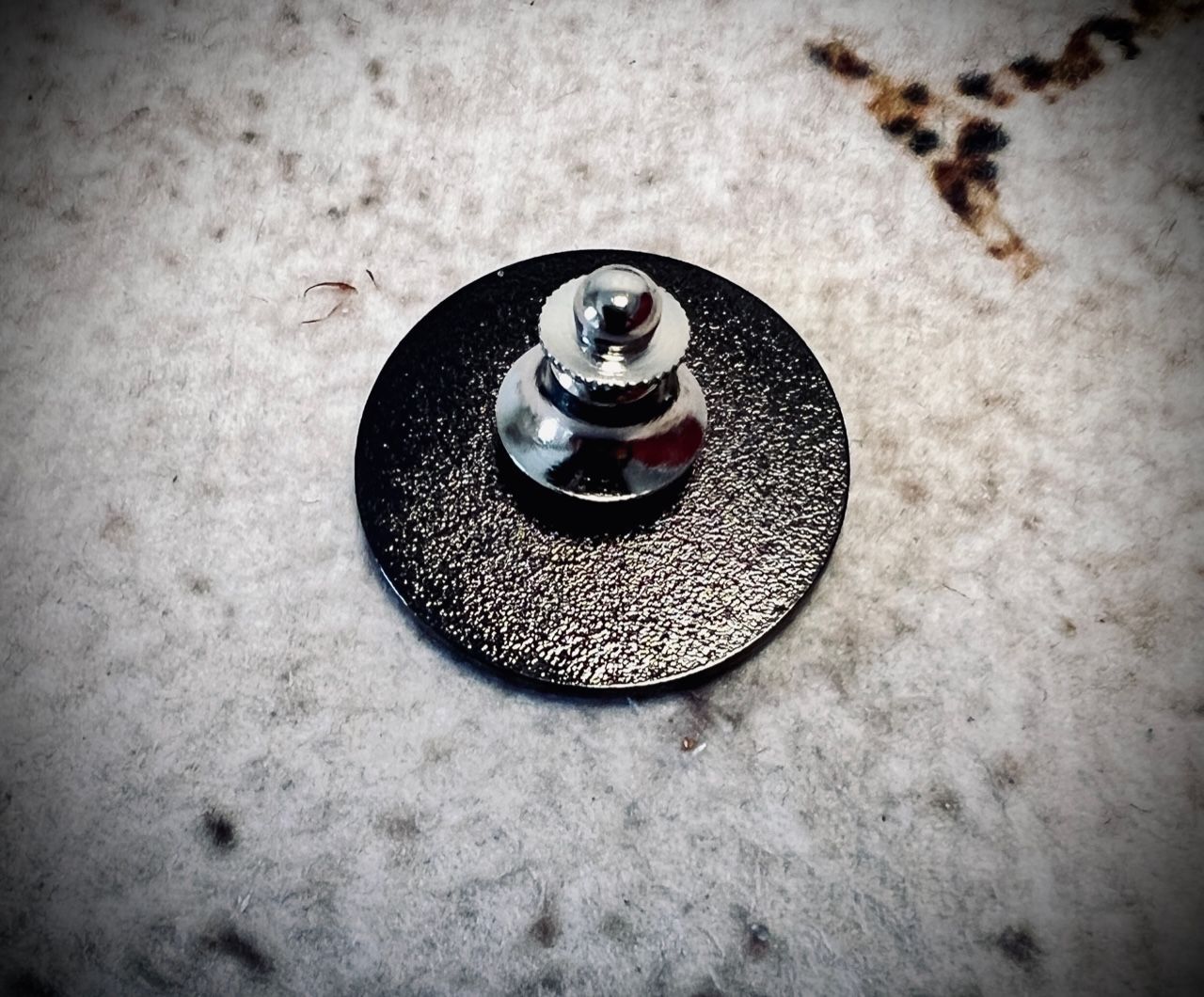 Close-up of a black circular metal piece with a silver stud on a speckled stone surface