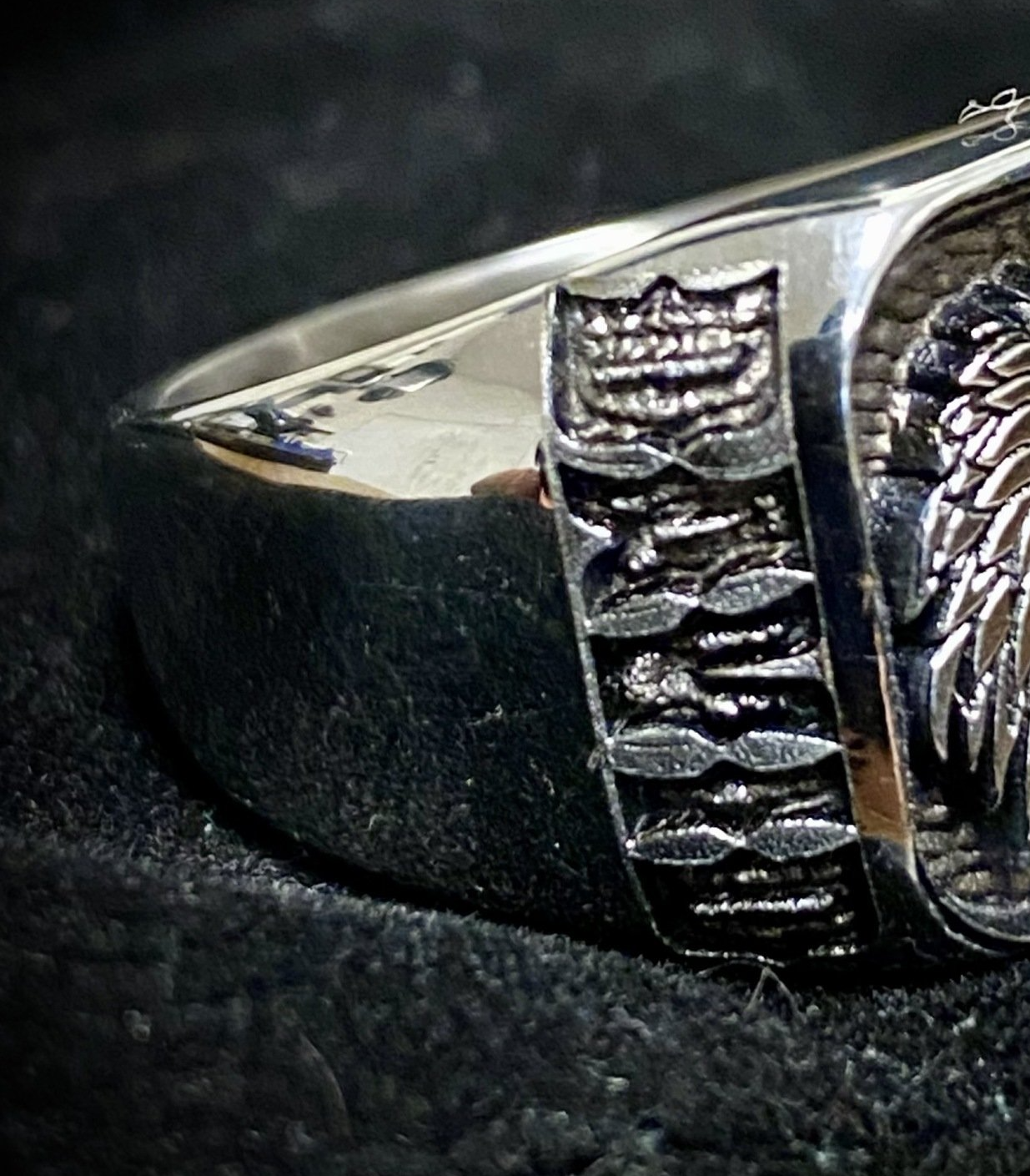 Close-up of a silver ring with a textured black and silver design on a dark fabric background