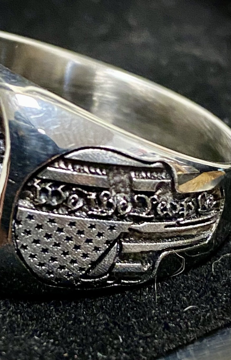 Close-up of a silver ring with a textured oval design on a dark fabric background