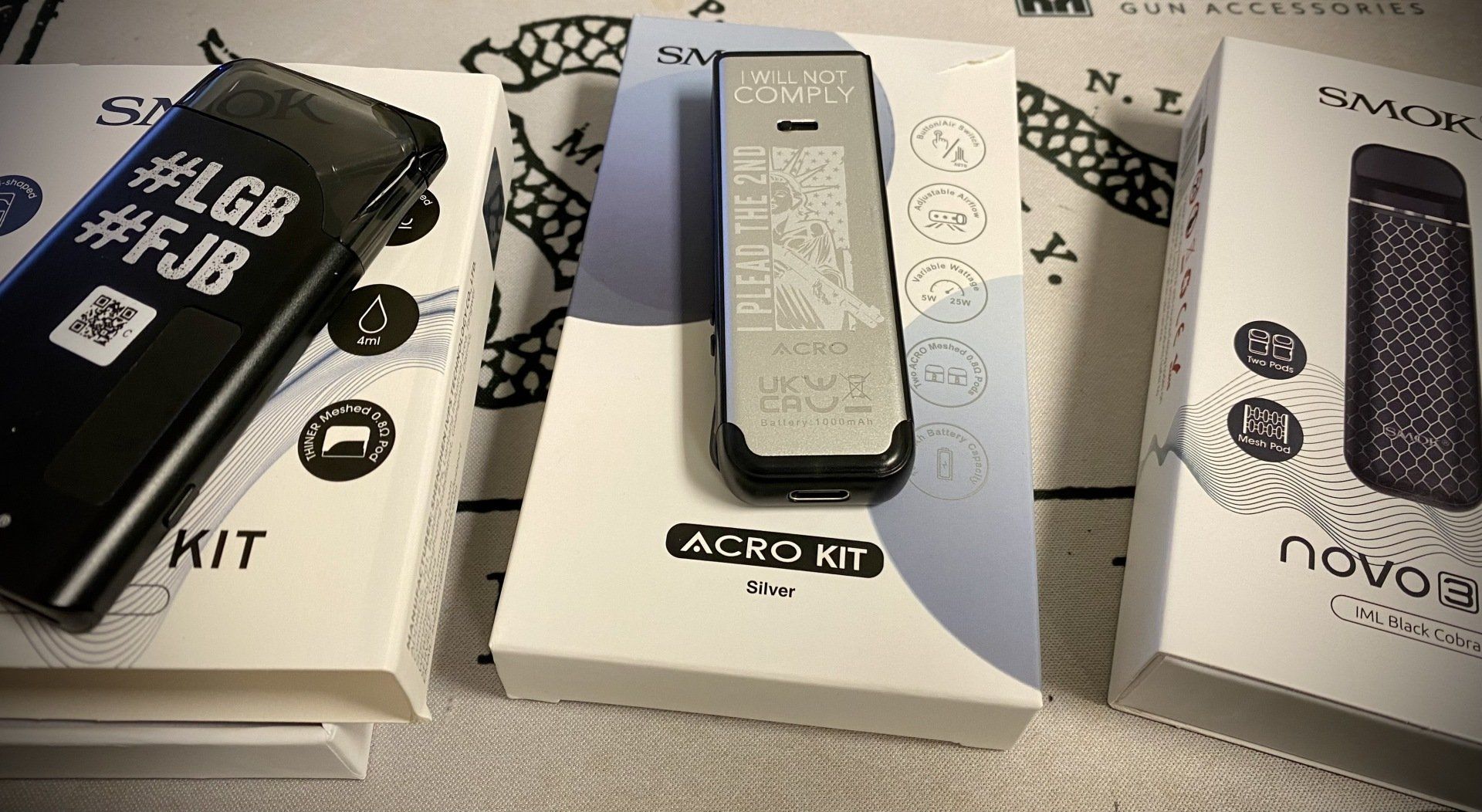 Three portable devices with English text rest on patterned boxes, one black, one silver, and one dark purple.