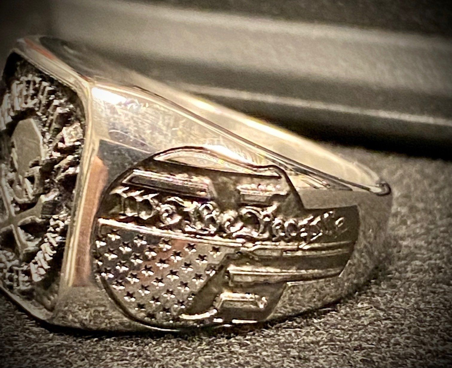 Close-up of a silver ring with an engraved car design on a dark fabric surface