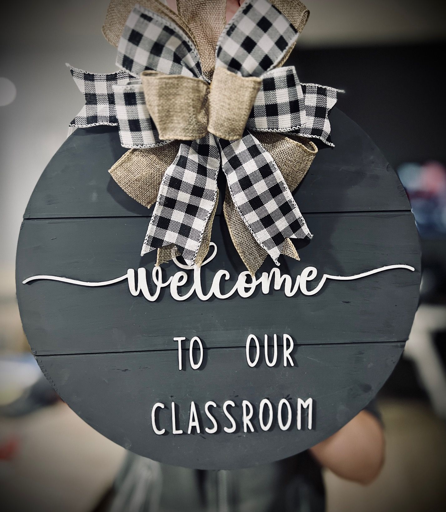 Black round classroom sign with buffalo plaid bow and twine reading “welcome to our classroom”