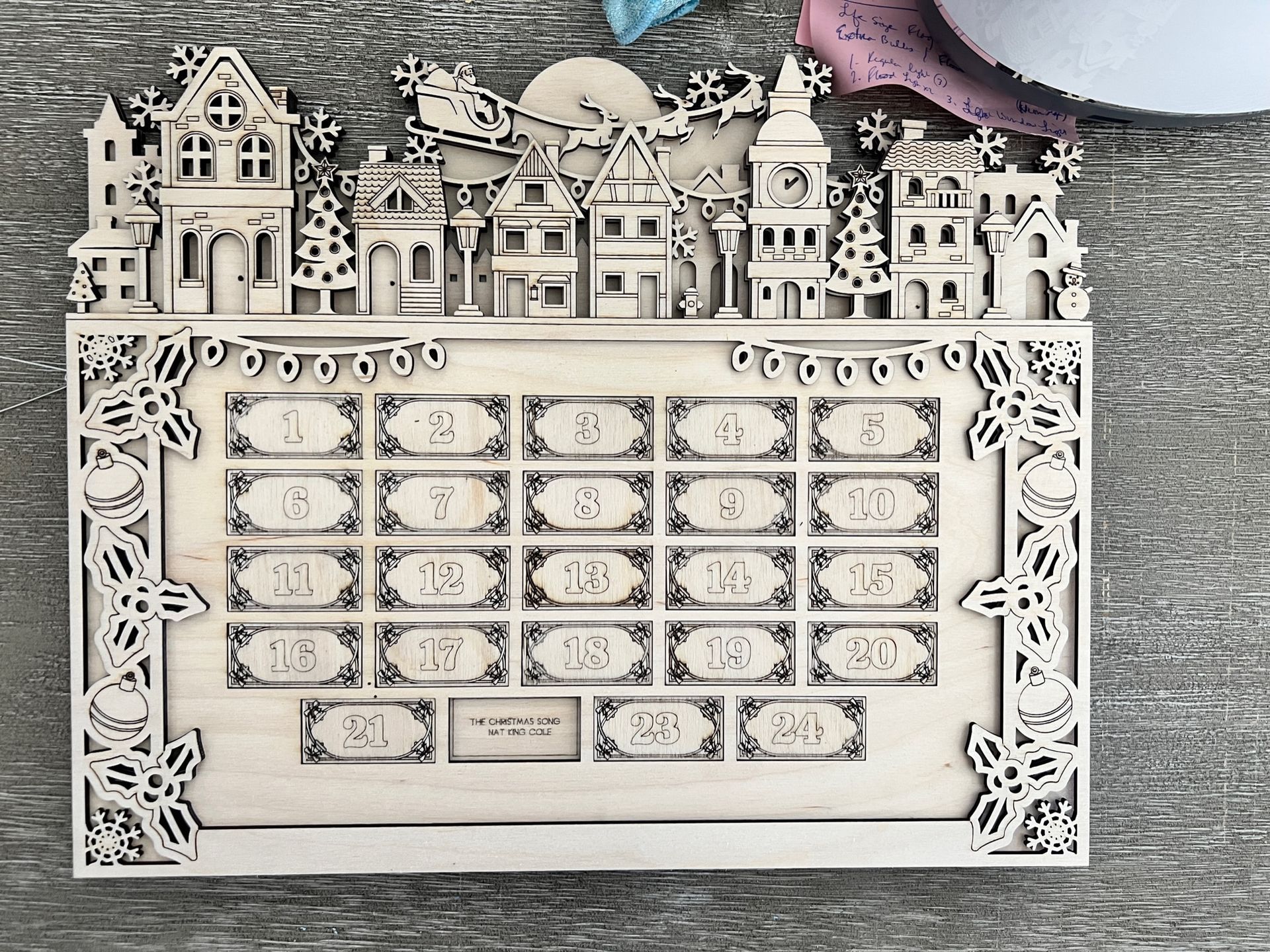 Decorative white pop-up winter village above a blank monthly calendar grid on a textured gray background
