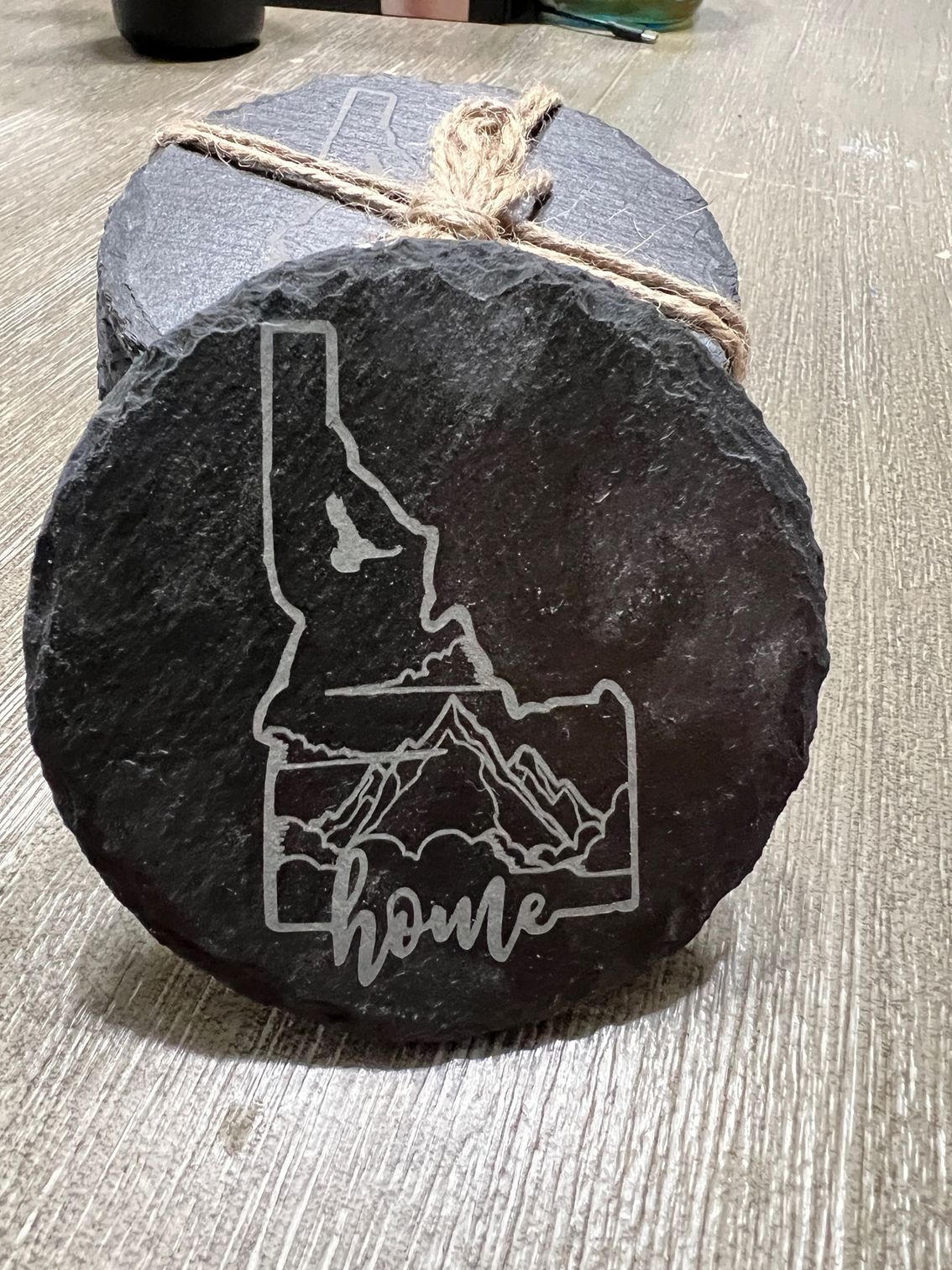 Black round stone with Idaho outline and the word “home” etched on a tabletop.