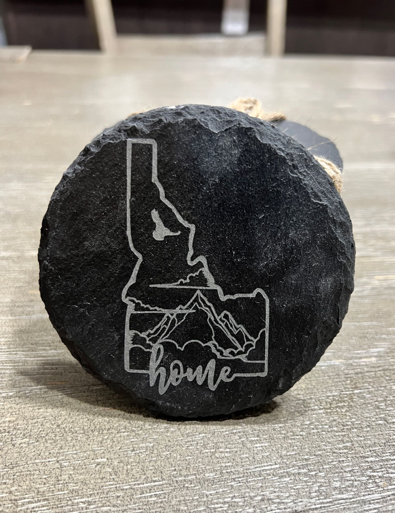 Black round rock with white outline of Idaho and the word “home” on a gray tabletop