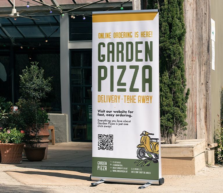 Tall garden pizza delivery sign on a sidewalk outside a restaurant, with yellow and green text.