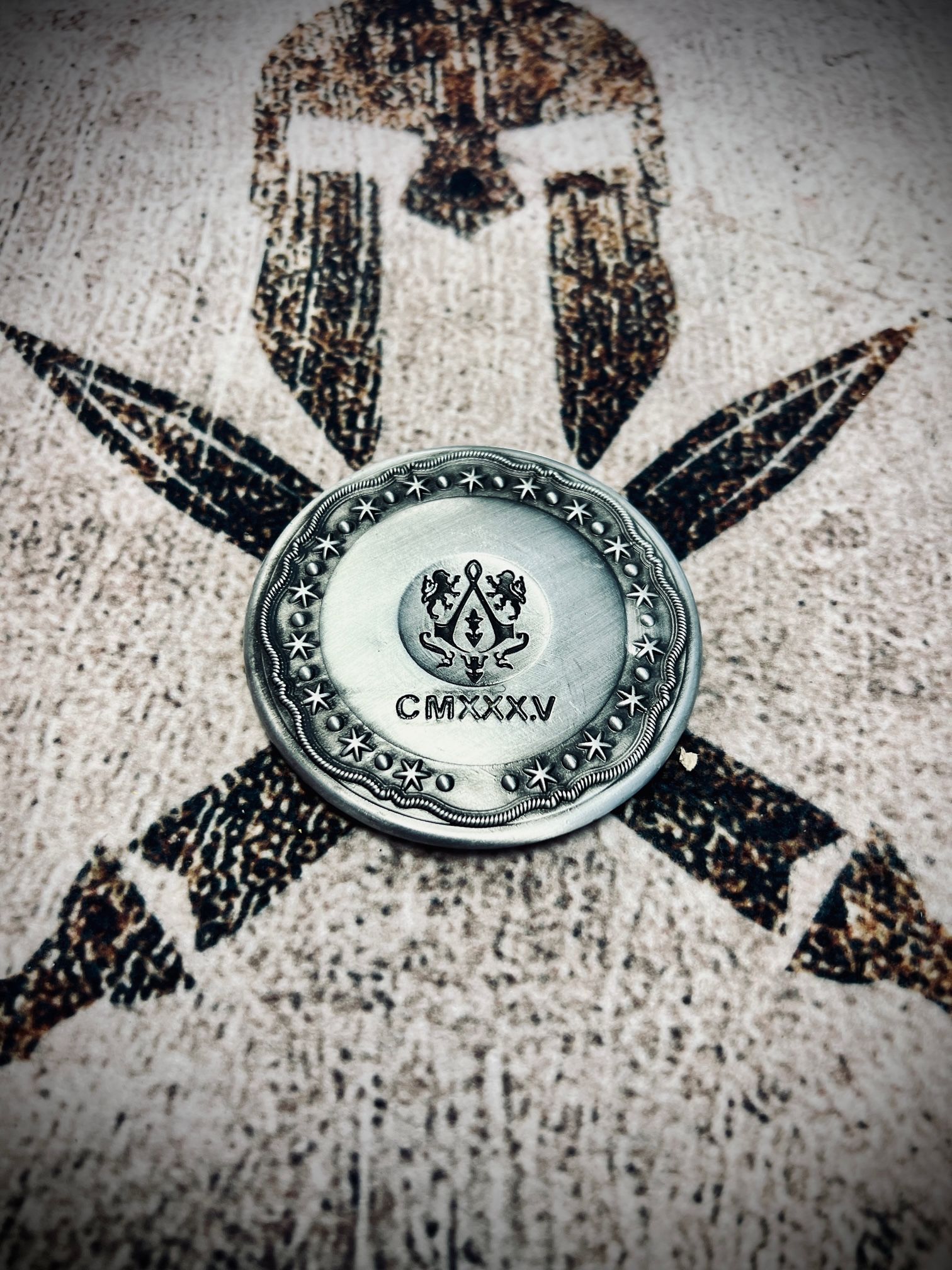 Round metal medallion on a speckled surface with a black-and-white star-like design beneath it