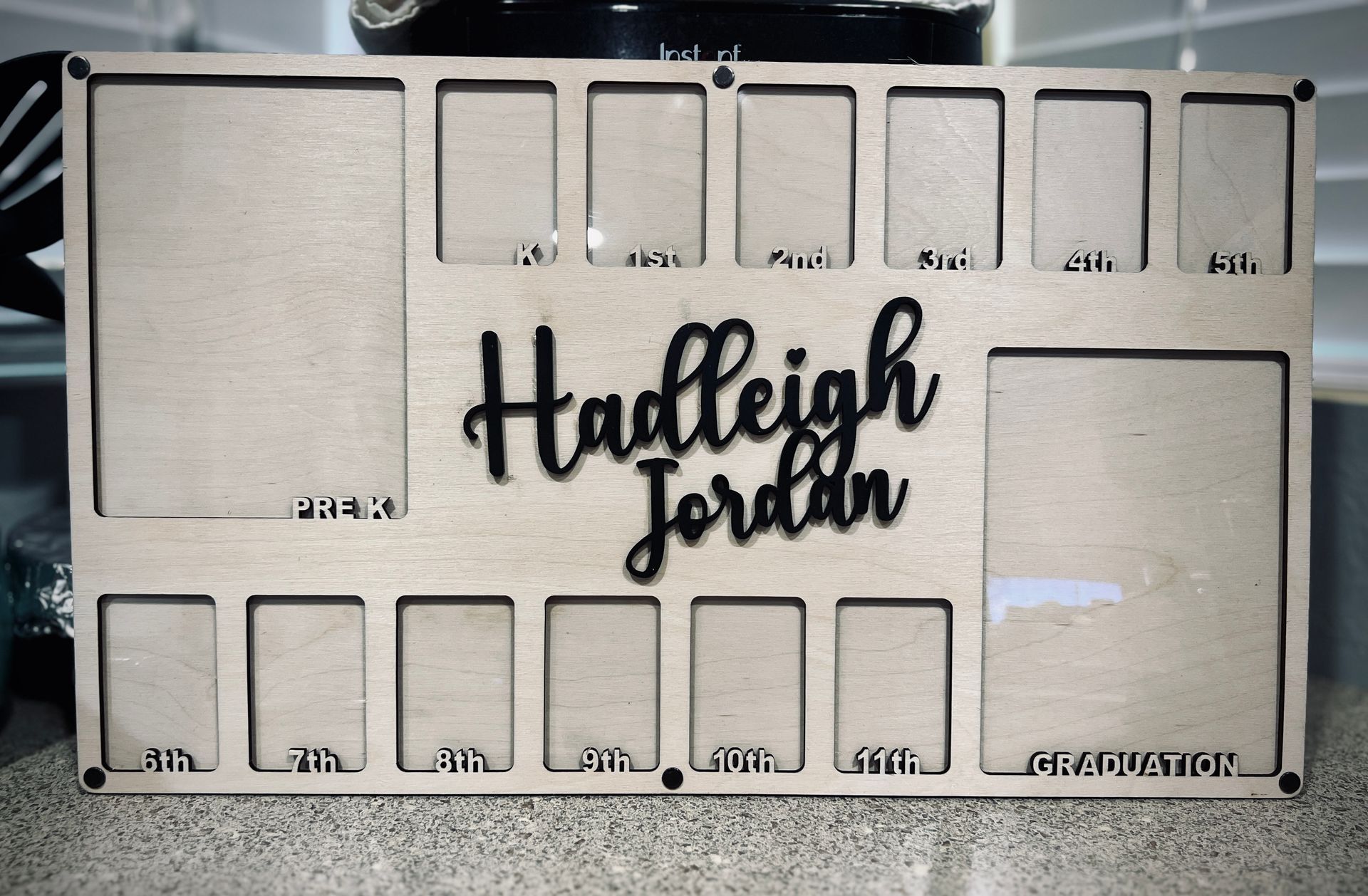 Personalized gray photo mat with “Hadleigh Jordan” in the center and multiple small photo slots around it