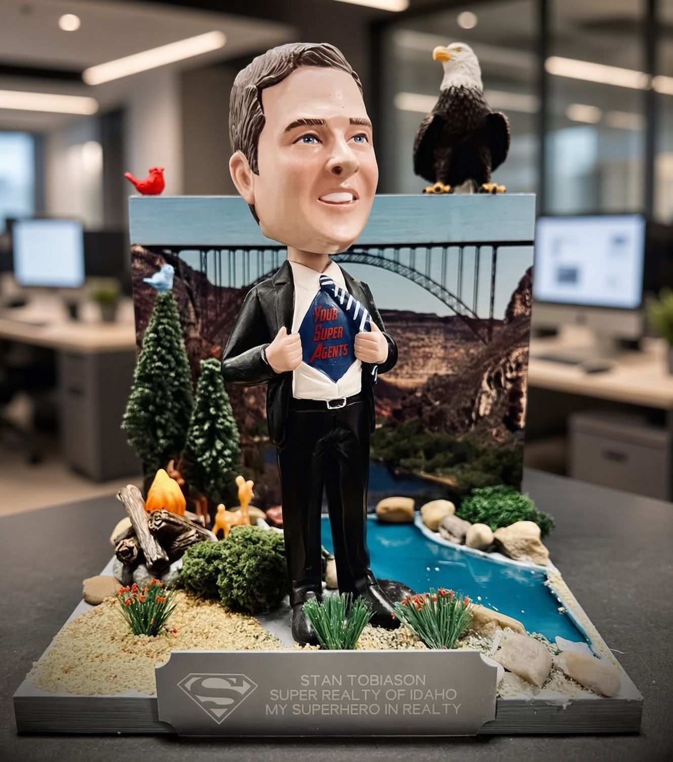 Bobblehead figure in a suit holding a plaque, with an eagle and scenic bridge display behind it.