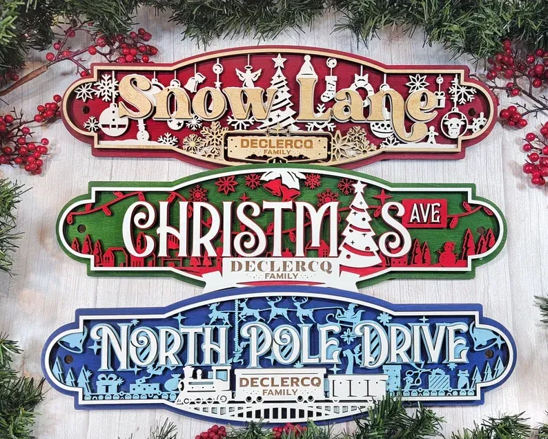 Three festive signs stacked vertically: Home Lane, Christmas Ave., and North Pole Drive, in red, green, and blue