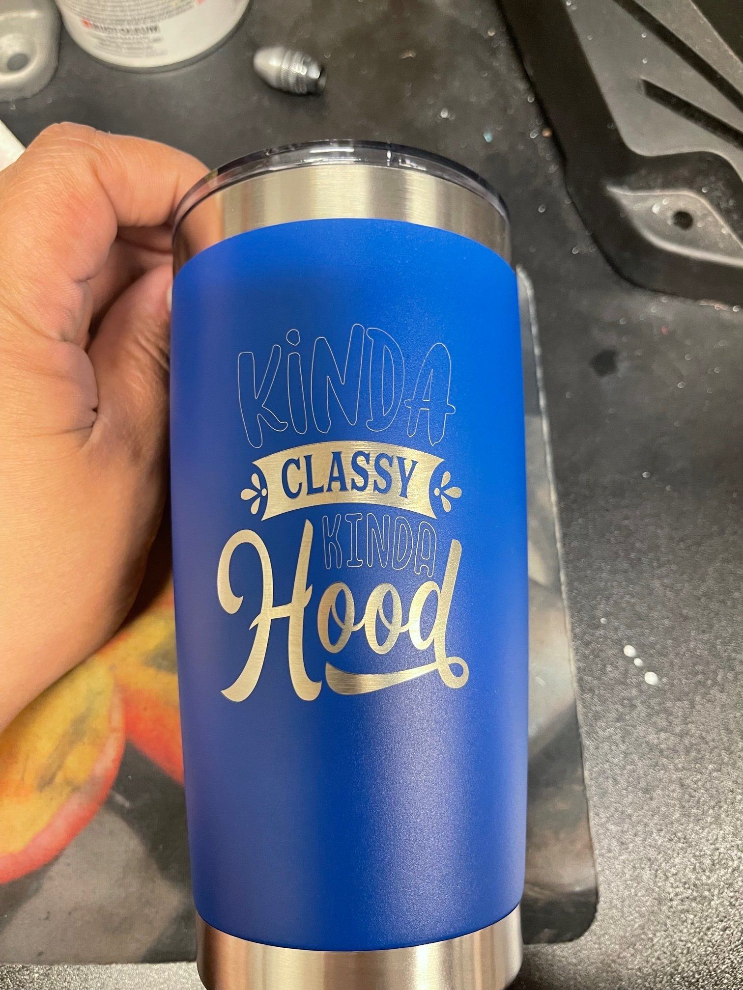 Blue tumbler with gold “Classy Hood” lettering, held in a hand over a countertop.