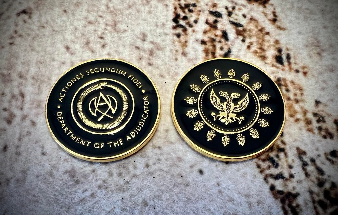 Two black and gold coins, one with a symbol, the other with an eagle, both with text around the edges.